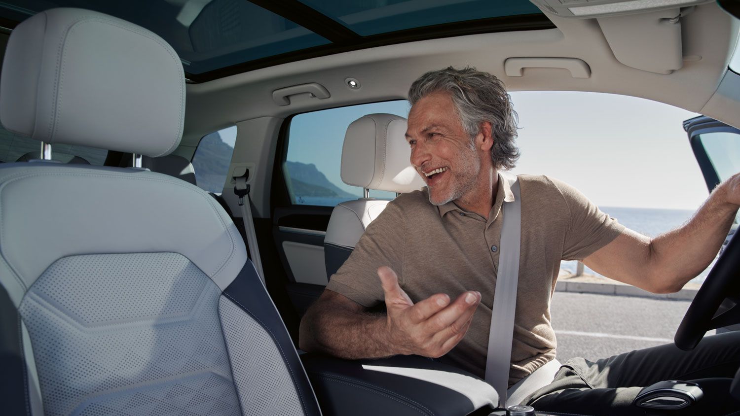 Ein Mann auf dem Vordersitz eines parkenden VW Touareg Elegance unterhält sich mit einer Person auf dem Rücksitz. 