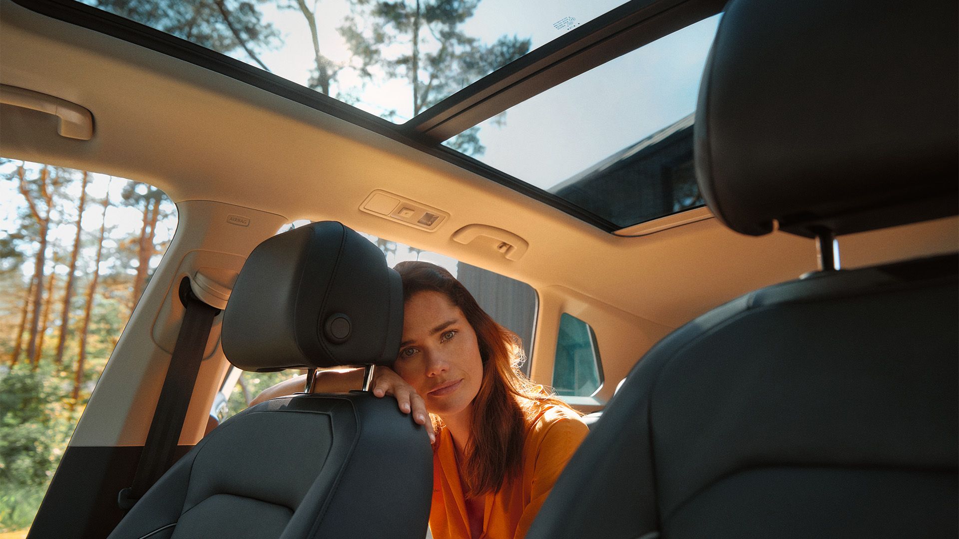 Frau sitzt auf der Rückbank des stehenden VW ID.3, lehnt an der Lehne des Beifahrersitz und schaut den Betrachter an