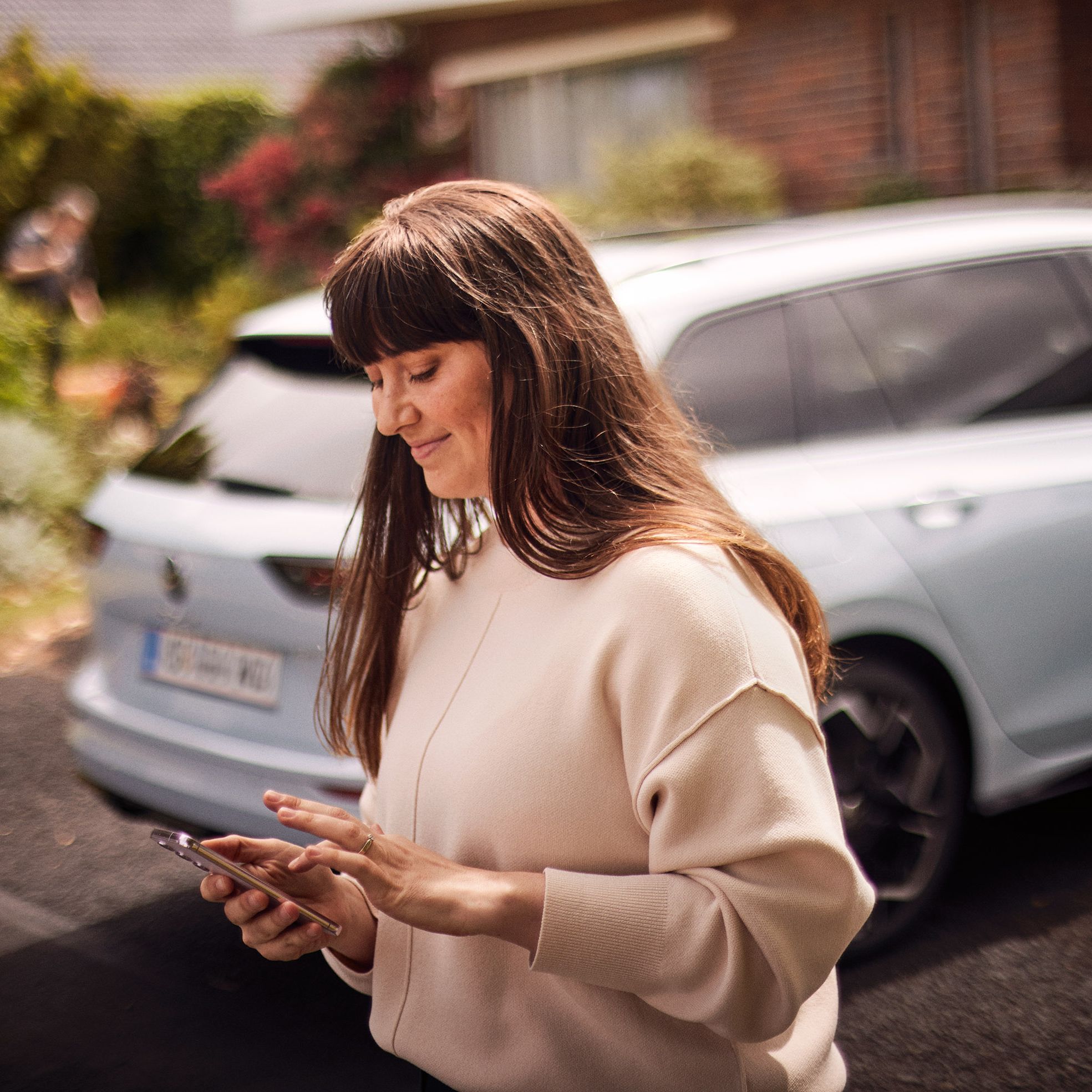 Frau steht vor VW Golf Variant und nutzt die Volkswagen App auf ihrem Smartphone
