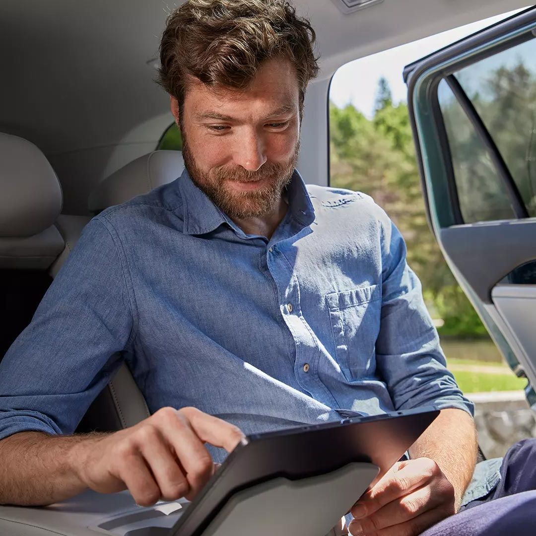 Mann sitzt auf Rückbank im VW Passat und bedient Tablet das in der Halterung befestigt ist