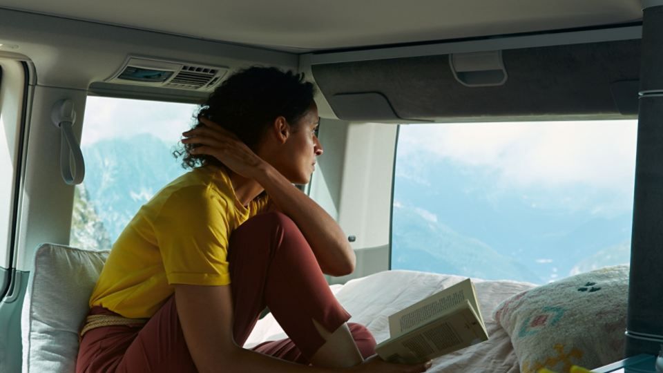 Eine Frau liest im Bett eines VW California 6.1