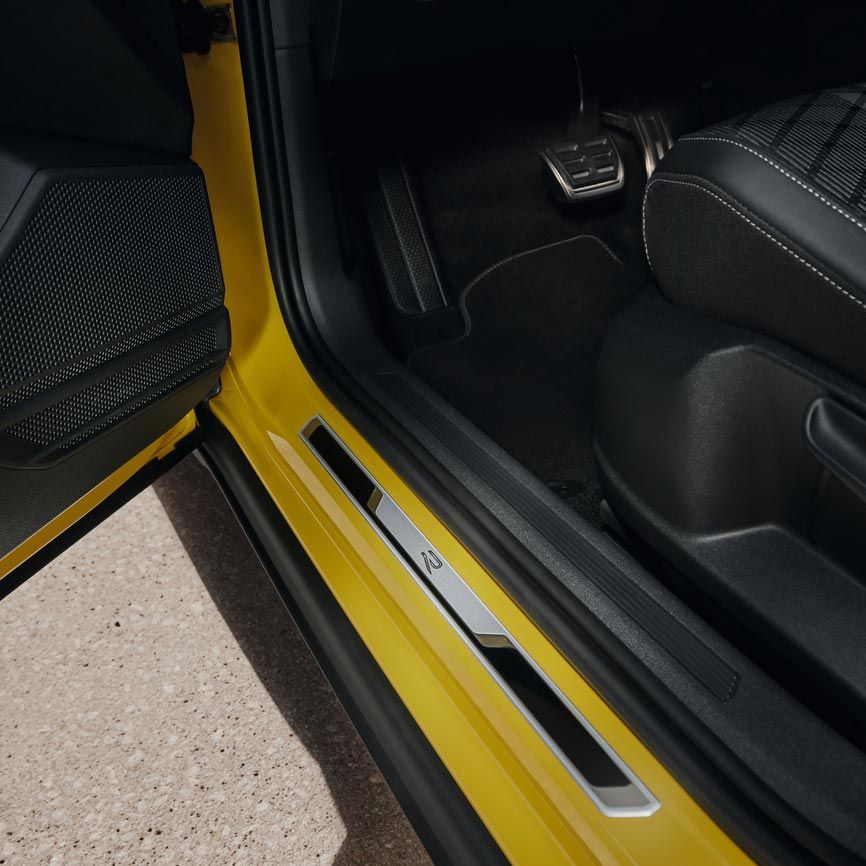 Blick auf unteren Teil des Fahrersitzes des gelben VW T-Cross bei geöffneter Vordertür mit der Einstiegsleiste aus gebürstetem Edelstahl.