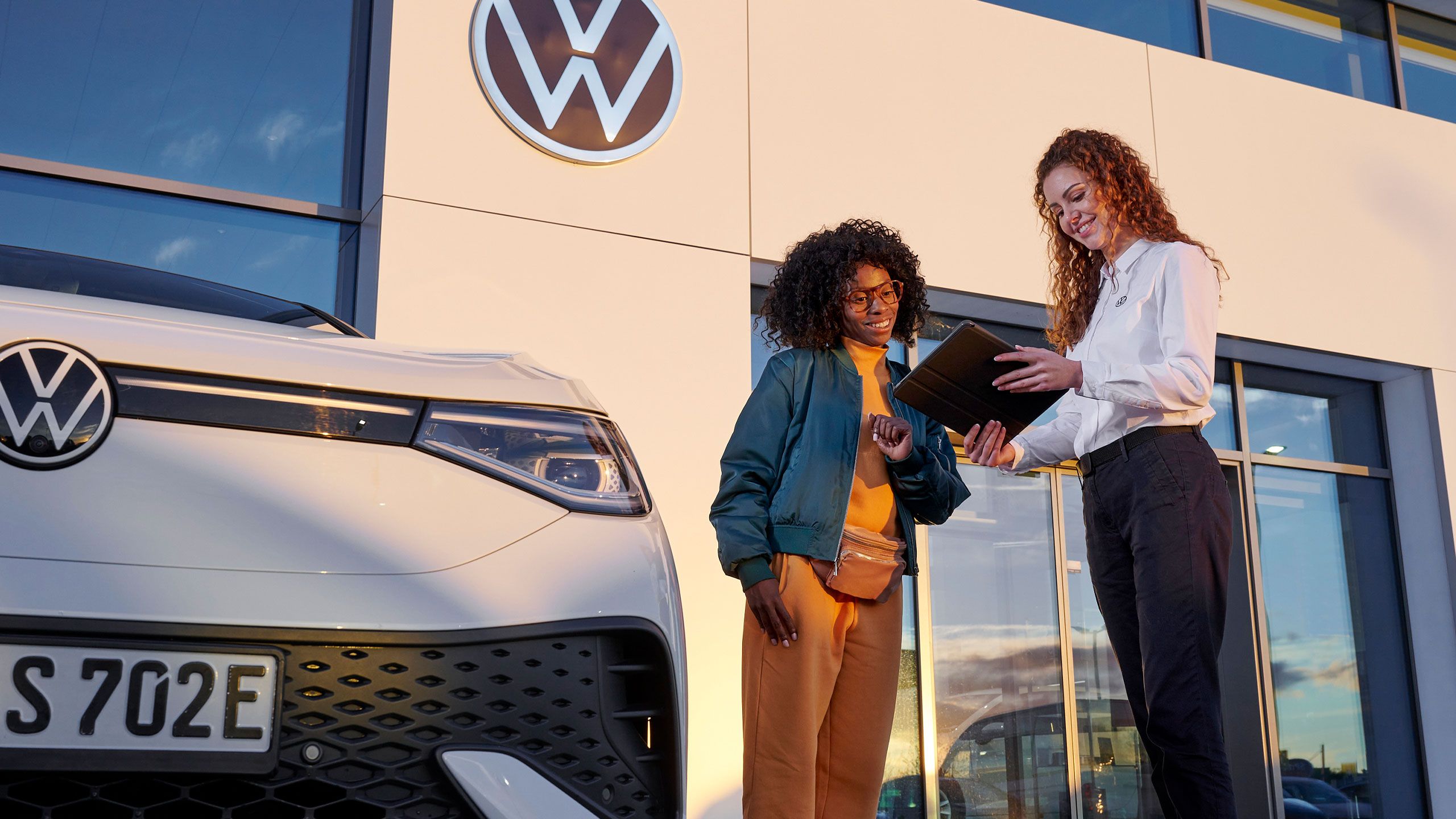 Eine VW Service MItarbeiterin mit einer Kundin vor einem Volkswagen Servicebetrieb
