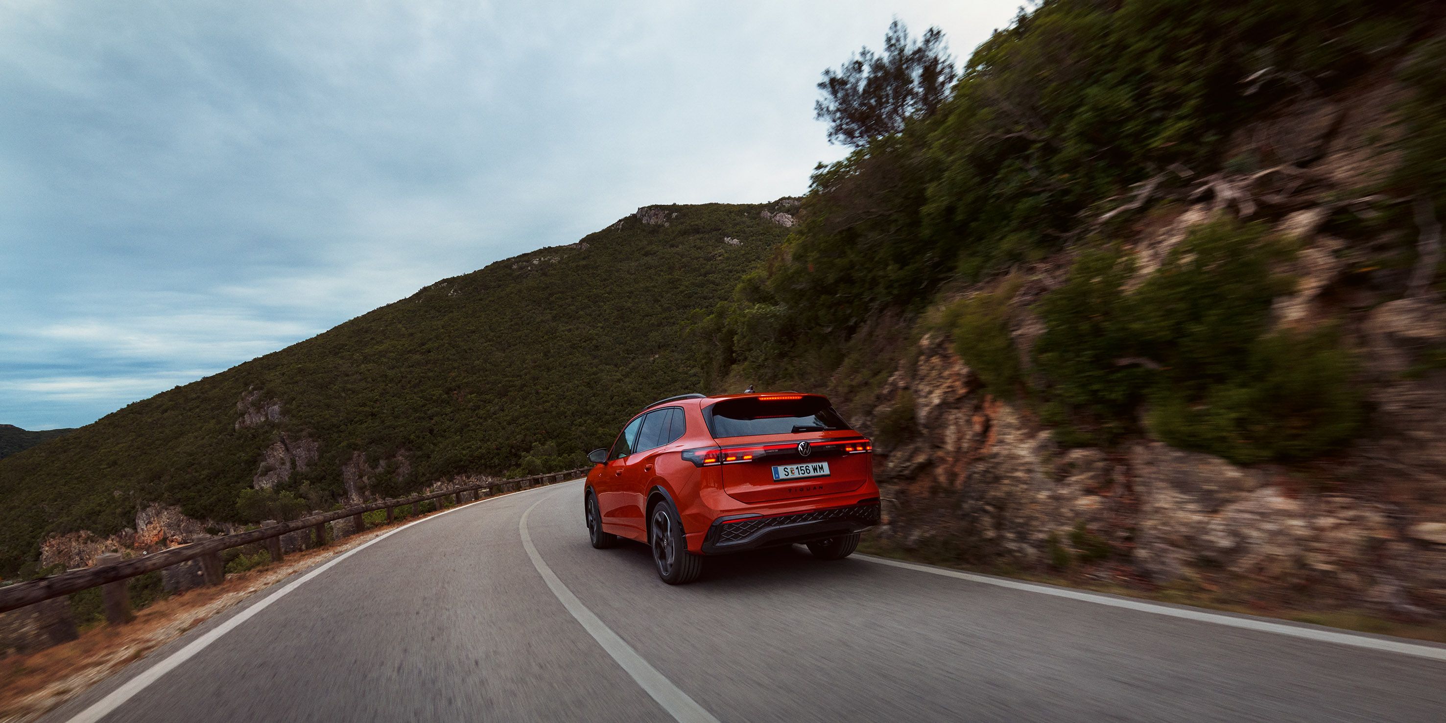 Roter VW Tiguan in Heckansicht fährt durch eine bergige Landschaft.