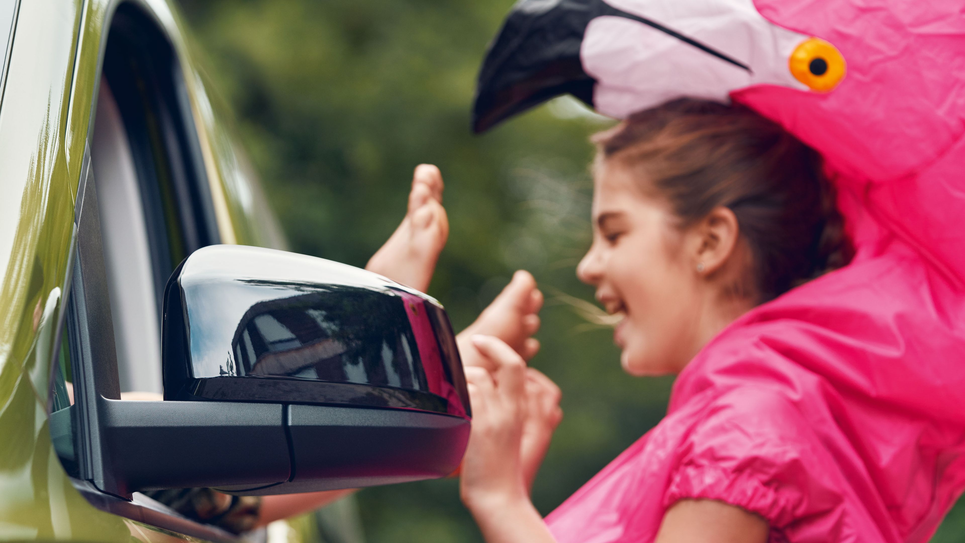 Ein junges Mädchen in einem Flamingokostüm am geöffneten Fenster eines VW Caddy.