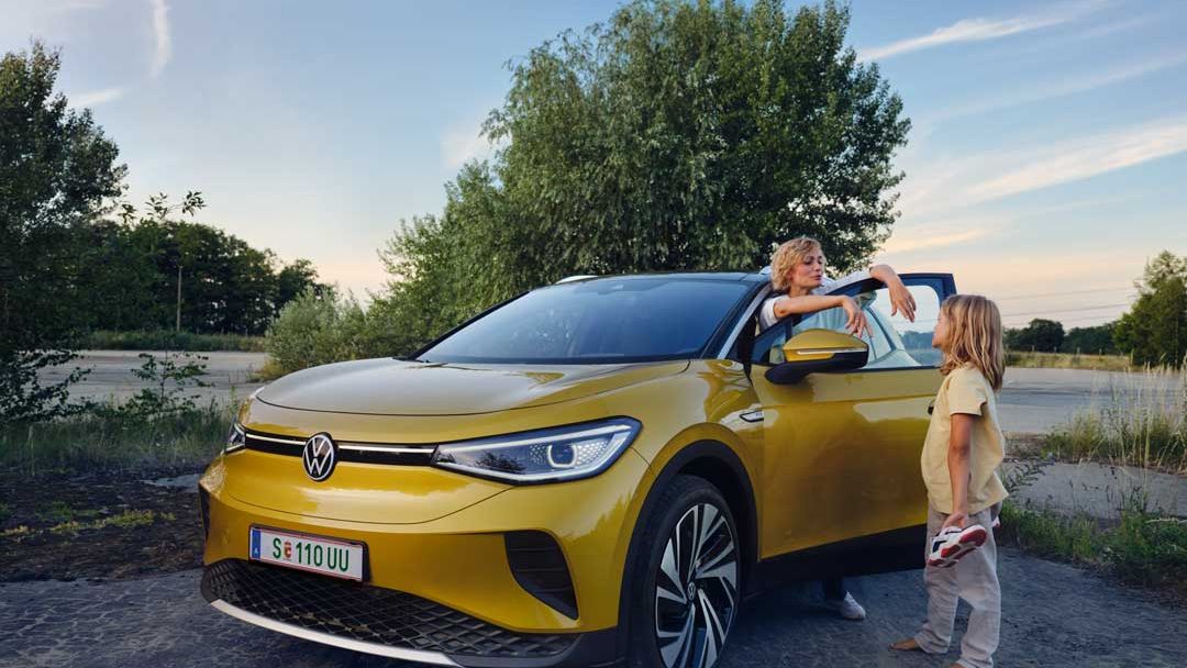 Eine Frau lehnt an einem gelben Volkswagen ID.4 und unterhält sich mit einem Kind