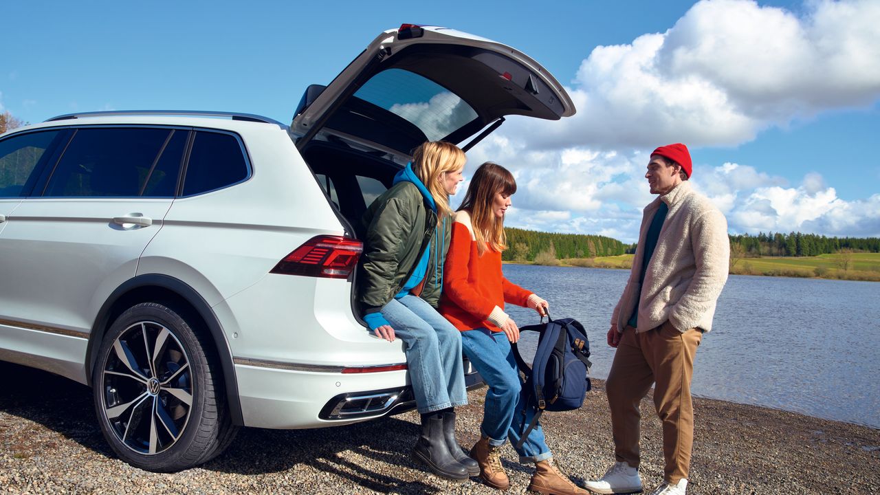 Zwei Frauen sitzen auf der Kofferraumkante des VW Tiguan Allspace und unterhalten sich mit einem Mann