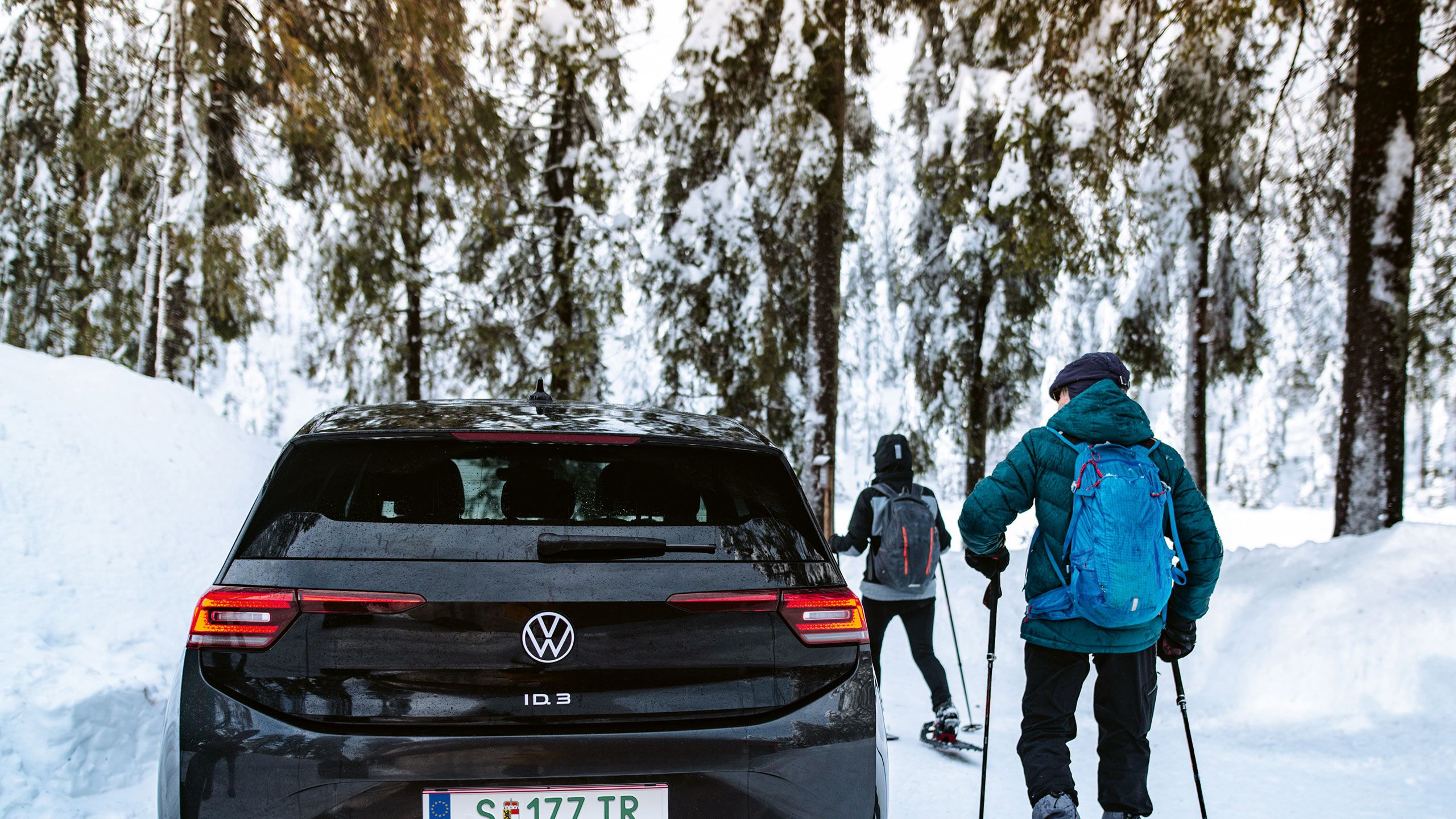 Ein schwarzer VW ID.3 steht in einer Schneelandschaft während zwei Menschen Skifahren