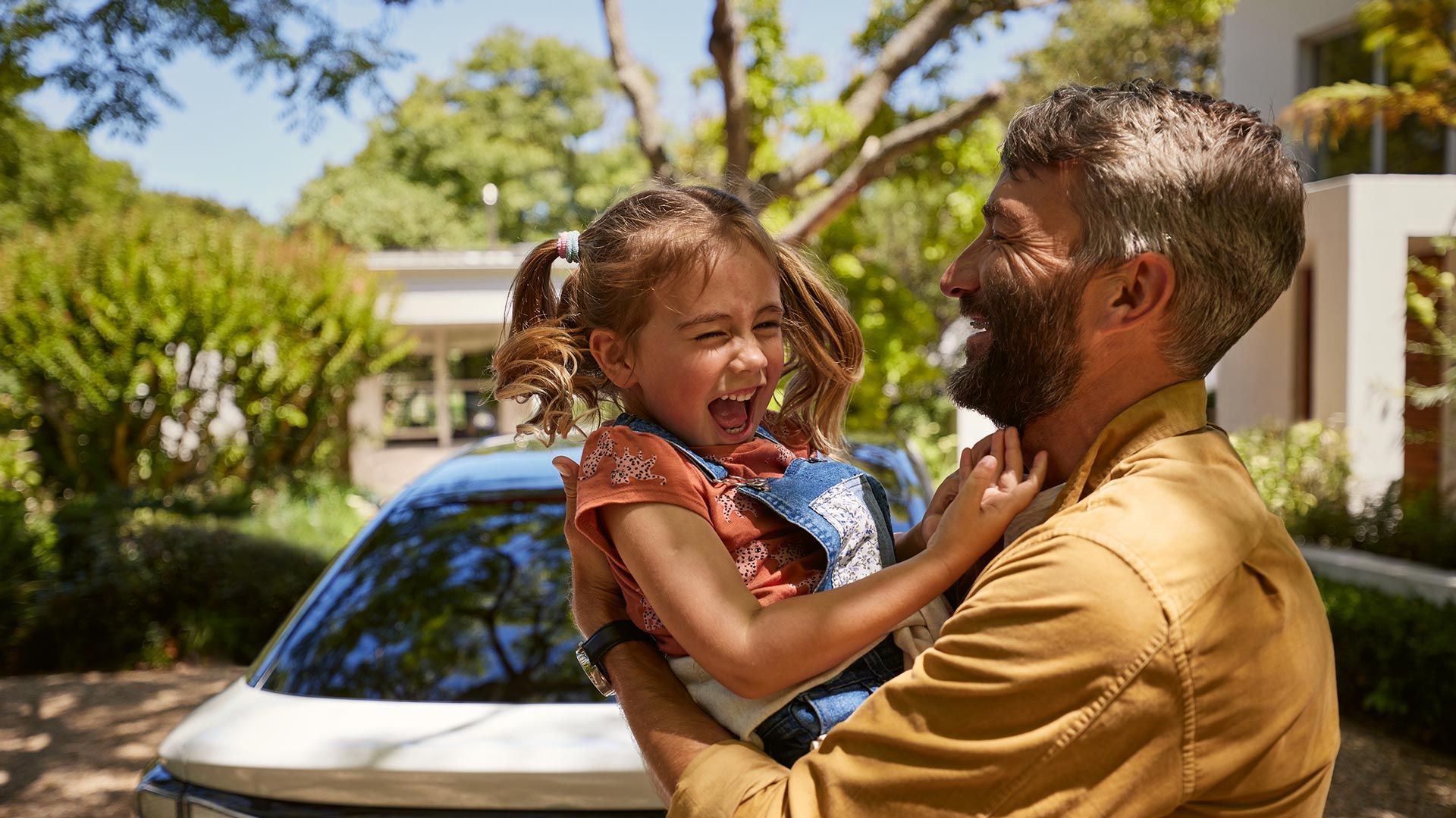 Ein Vater hält Kind im Arm, beide lachen, man sieht das Heck des VW ID.7