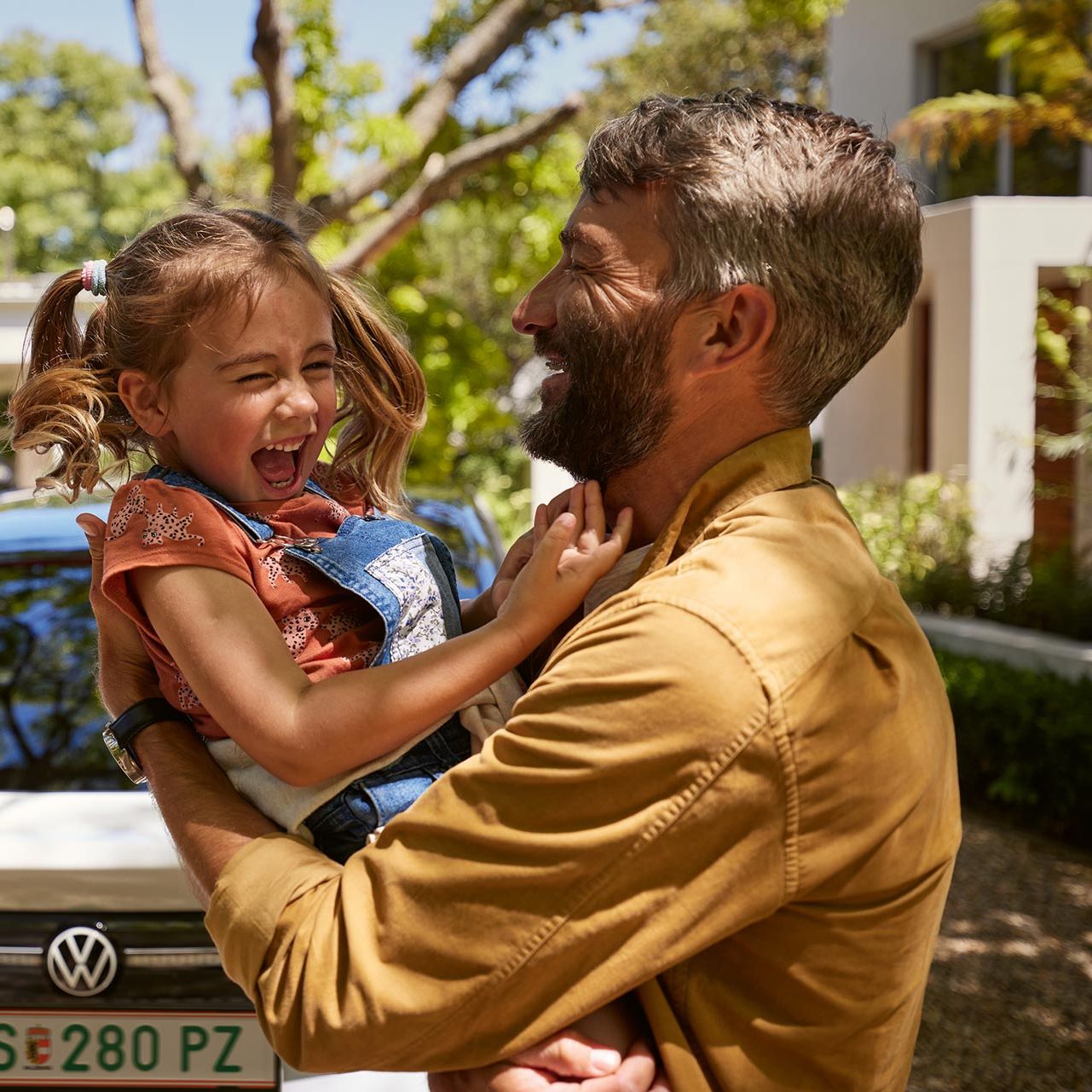 Ein Vater hält Kind im Arm, beide lachen, man sieht das Heck des VW ID.7