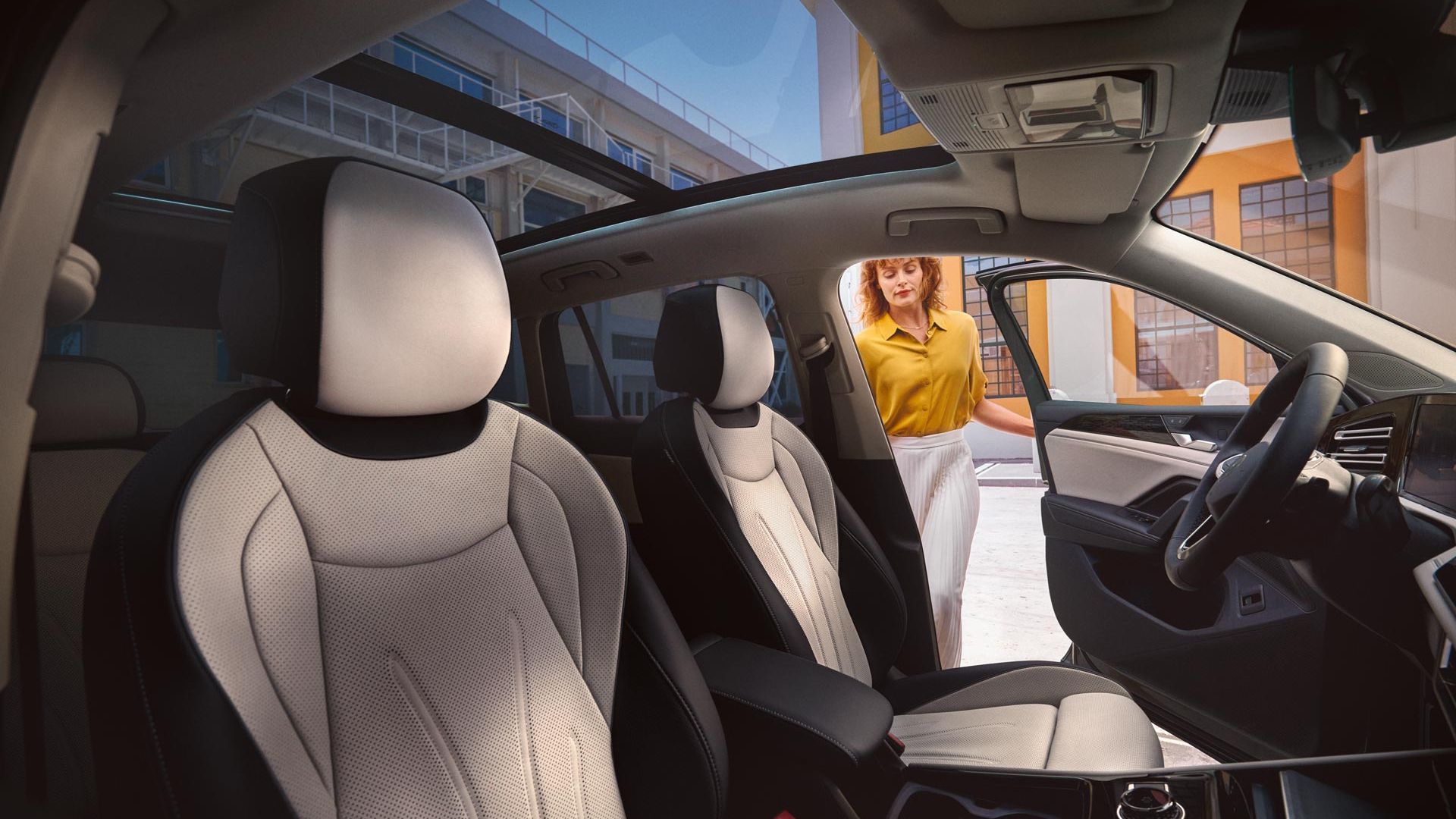 Innenansicht eines VW Tiguan mit Panoramadach und weißen Sitzen, Frau öffnet Fahrertür