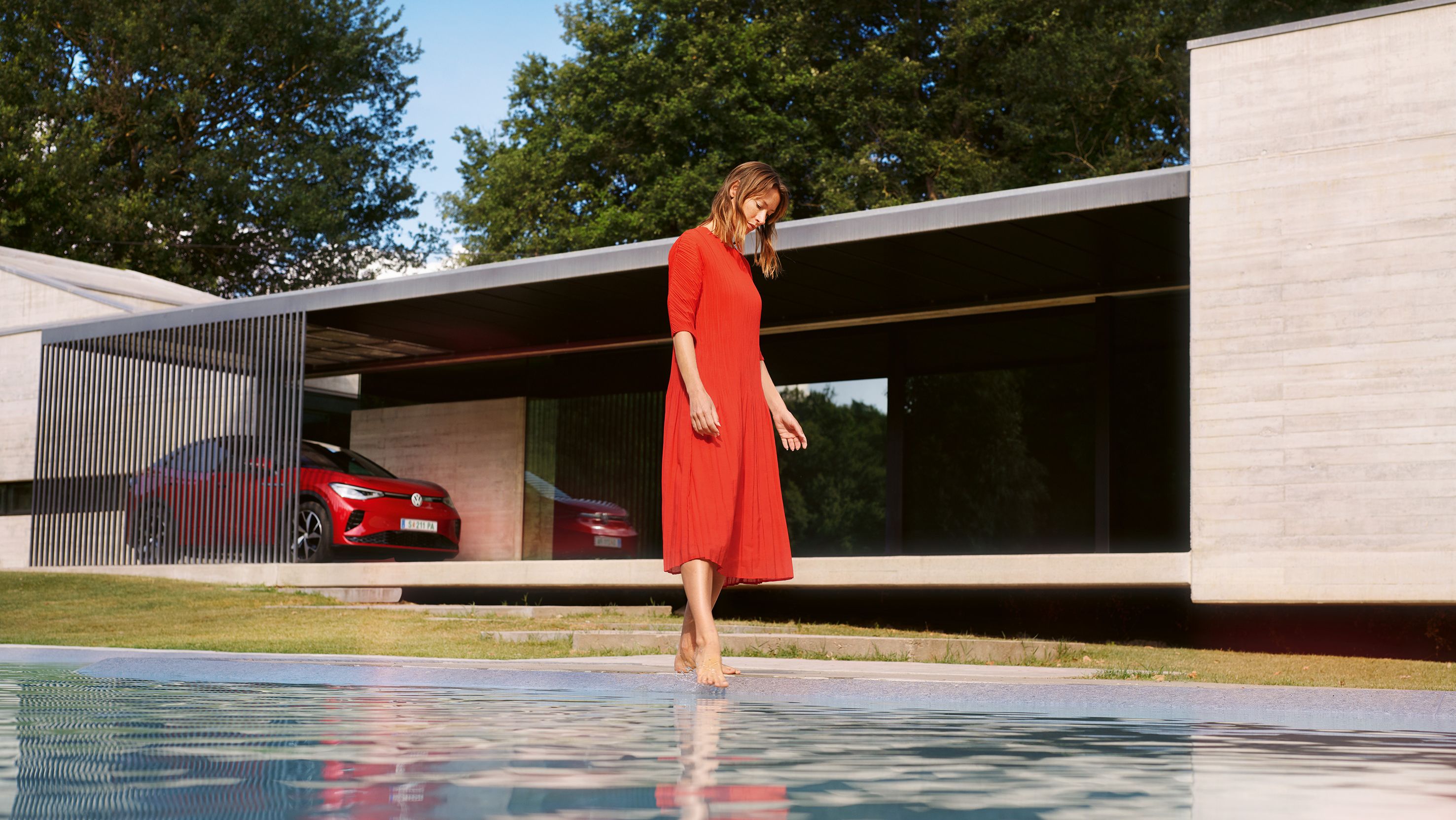Roter VW ID.5 GTX geparkt vor einem Haus. Eine Frau im roten Kleid am Pool.