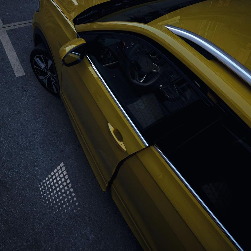 Die nur einen Spalt geöffnete VW T-Cross Fahrertür von oben, mit sichtbarer Lichtprojektion in der Dämmerung.