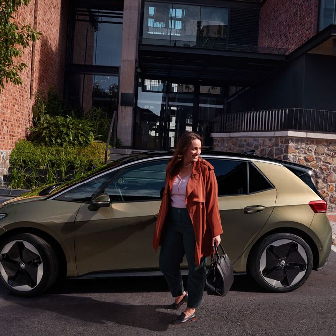 Eine Frau steht vor einem VW ID.3 in Olivgrün (Seitenansicht)