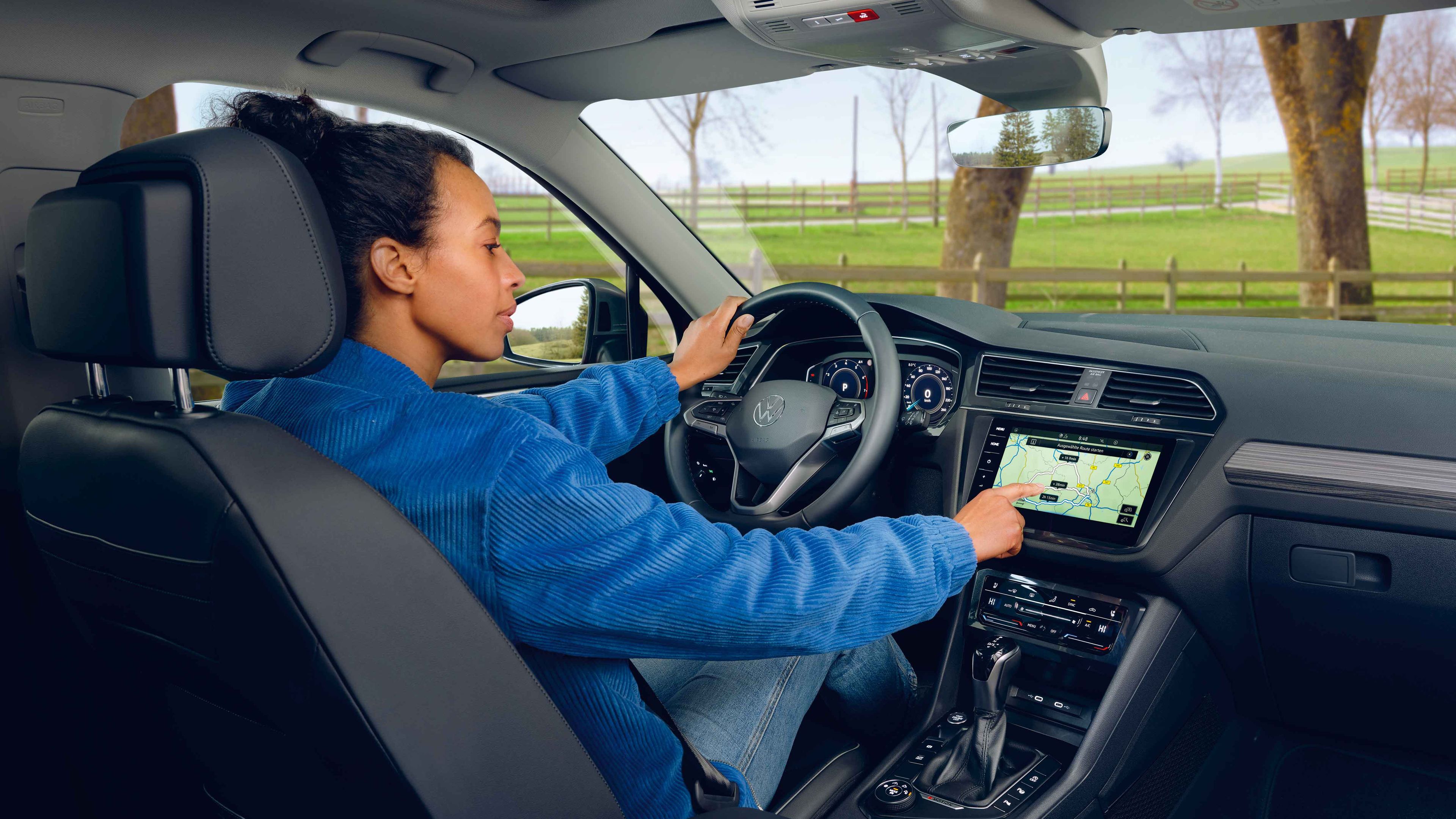 Eine Frau sitzt auf dem Fahrersitz des VW Tiguan Allspace und bedienet das Navigationssystem