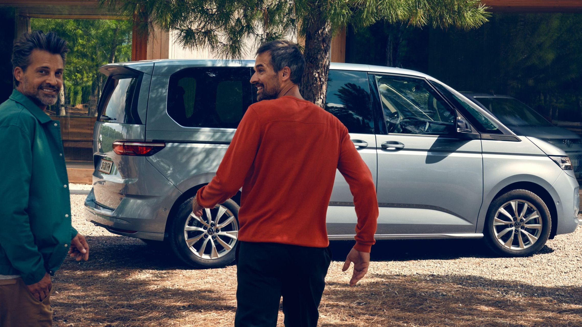 Zwei Männer laufen lachend auf den neuen VW Multivan Life T7 2021 zu.