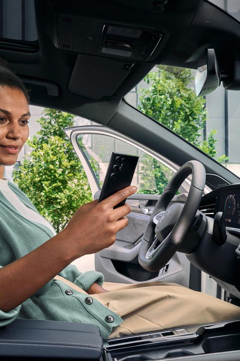 Frau sitzt im VW Passat R-Line und blickt auf ihr Smartphone