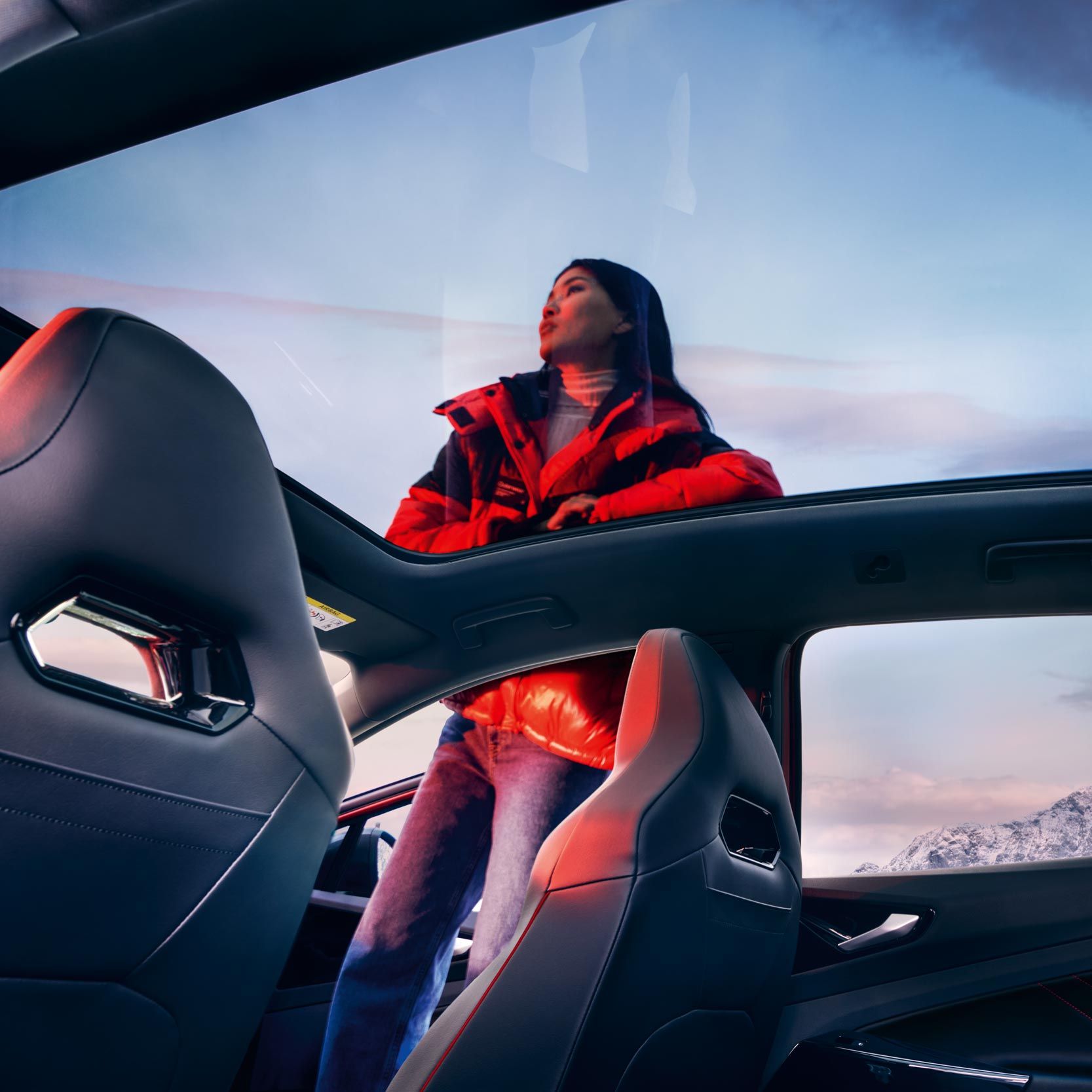 VW ID.4 GTX Blick von innen durch optionales Panoramaglasdach auf Frau neben dem Fahrzeug.