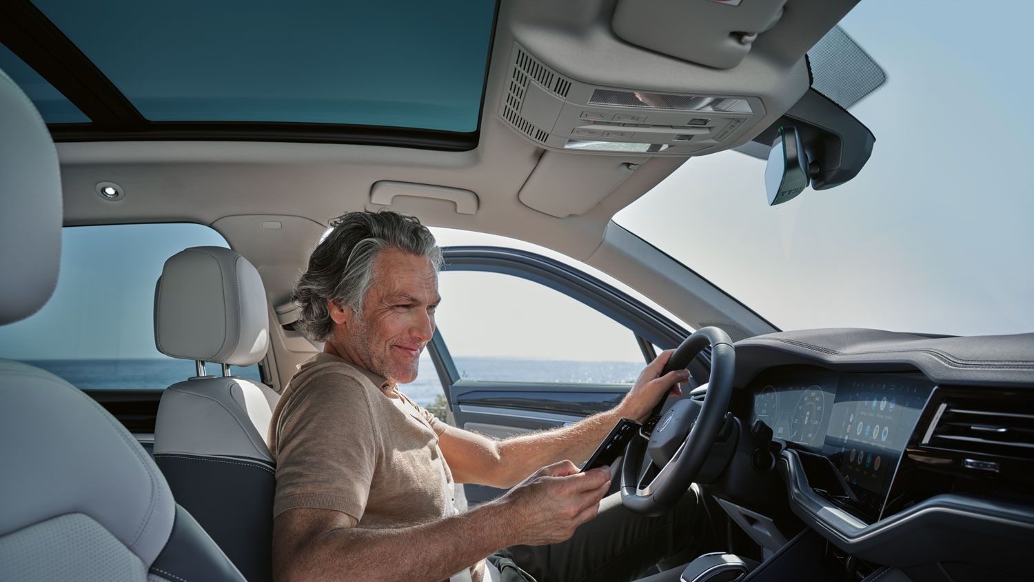 Ein Mann in einem parkenden VW Touareg Elegance verbindet sein Smartphone per Wireless App Connect mit dem VW Touareg Elegance.