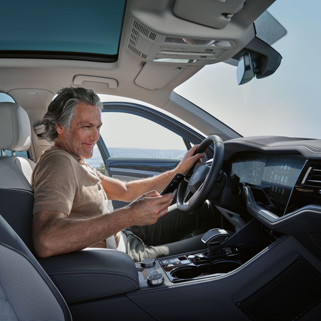 Ein Mann in einem parkenden VW Touareg Elegance verbindet sein Smartphone per Wireless App Connect mit dem VW Touareg Elegance.