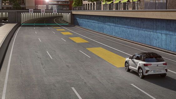 Ein Volkswagen T-Roc fährt auf einer leeren Autobahn Richtung Tunnel. Die Automatische Distanzregelung ACC wird mithilfe gelber Balken auf der Straße in unterschiedlichen Abständen abgebildet.