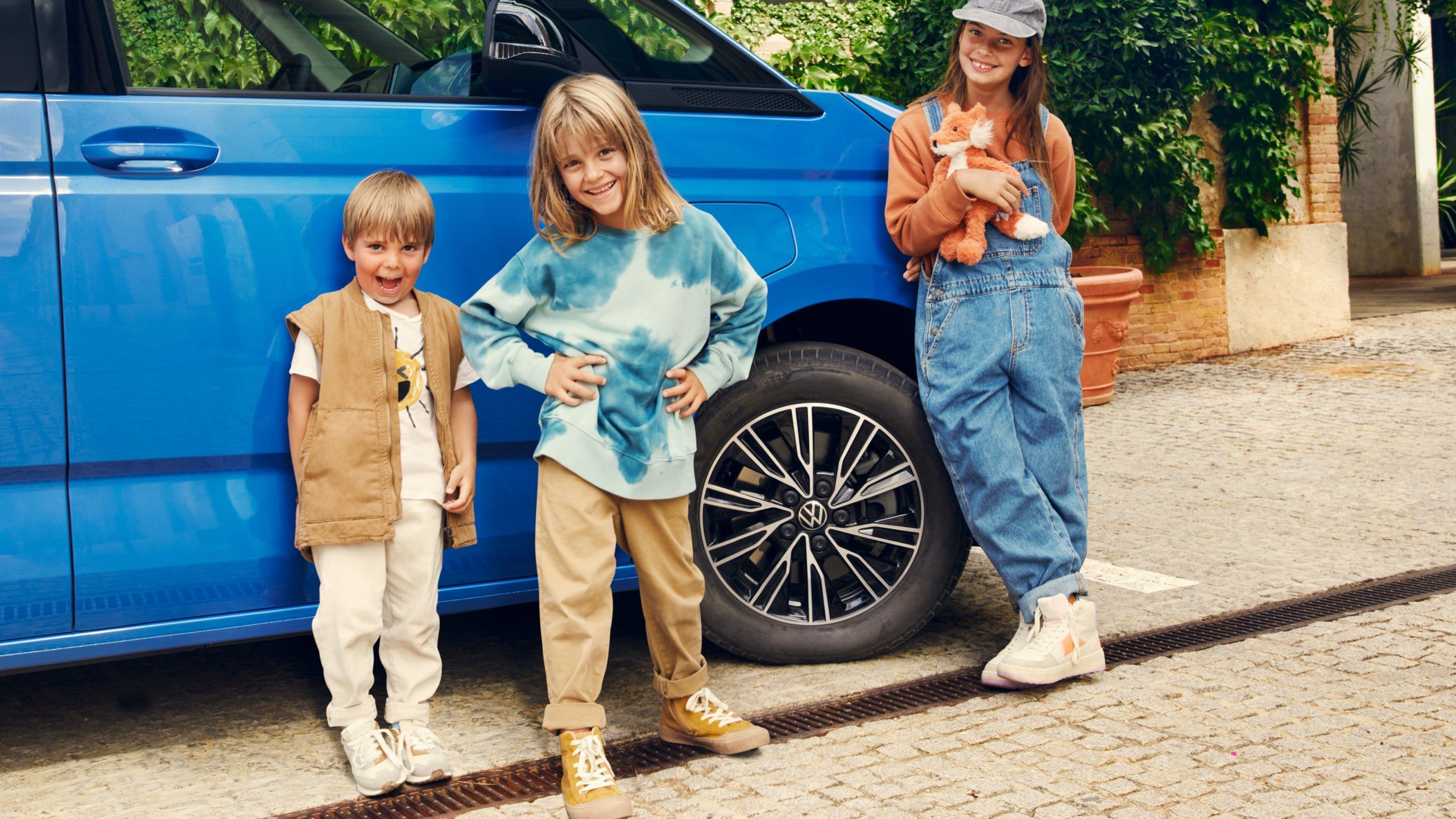 Drei Kinder stehen neben dem Vorderrad vom neuen VW Multivan T7 2021.