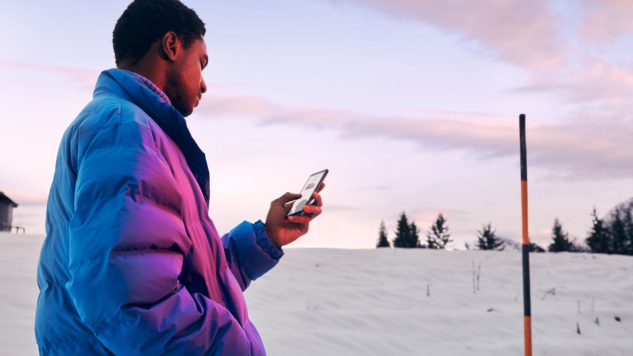 Mann in Winterlandschaft blickt auf ein Smartphone