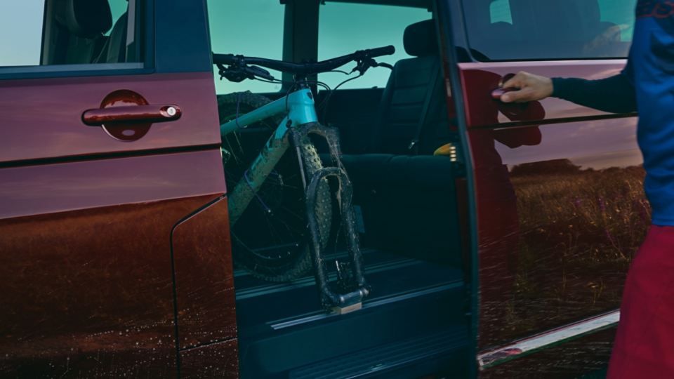 Ein Mann schließt die Schiebetüre des VW Multivan 6.1. Auf der Rückbank des Fahrzeuges sieht man ein Mountainbike. 