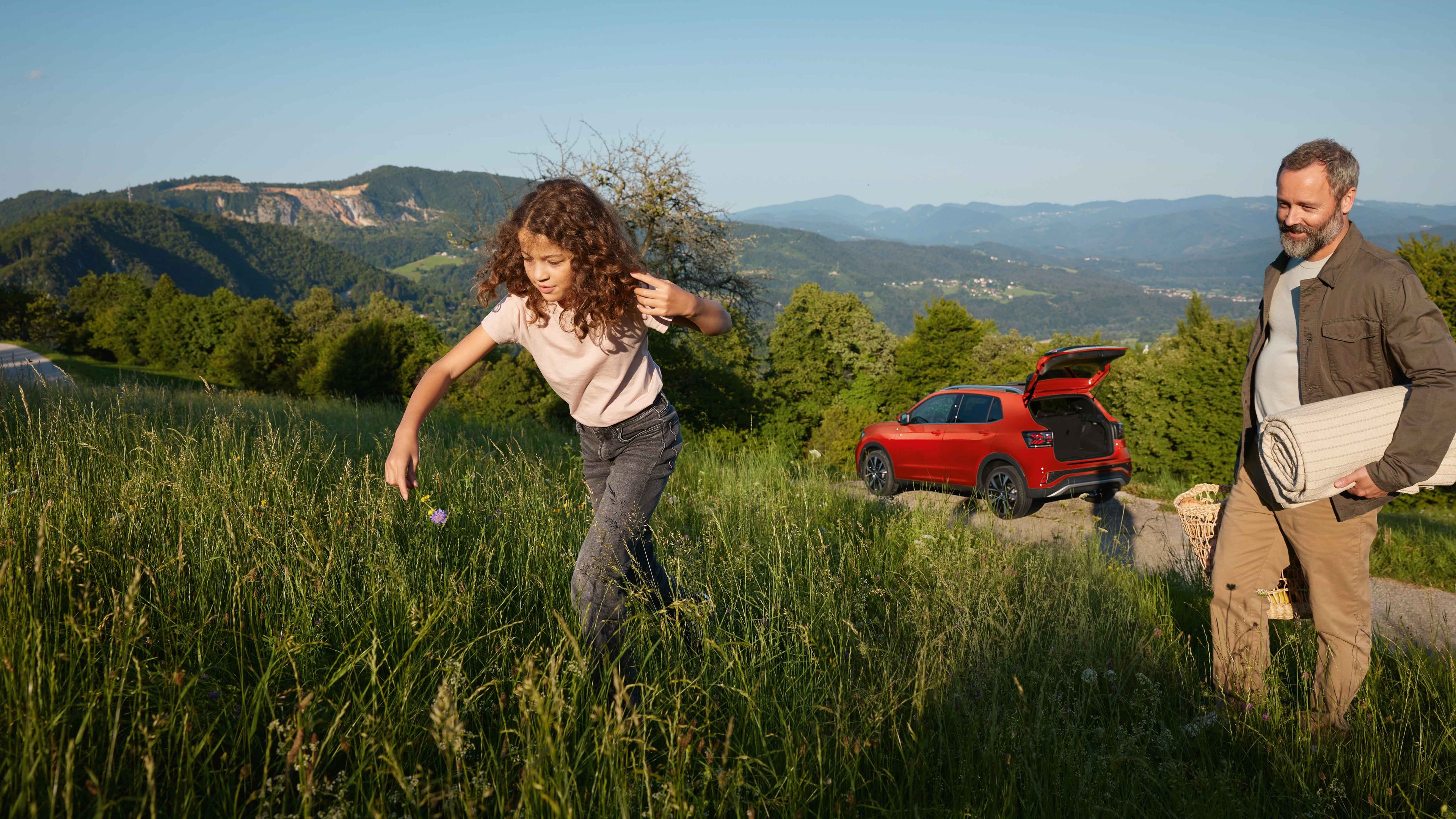 Vater und Tochter wandern in Berglandschaft, im Hintergrund sieht man roten VW T-Cross