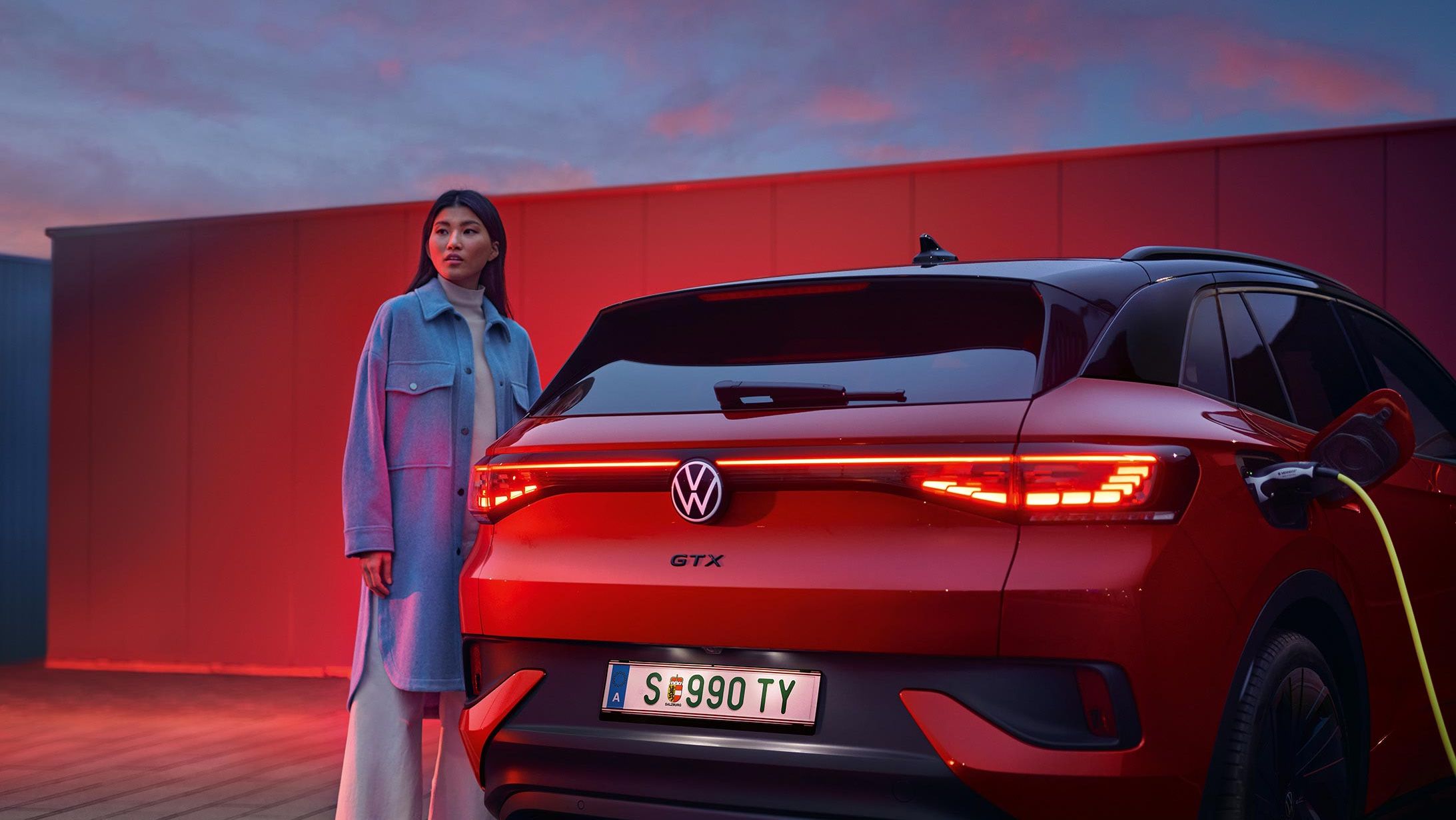 VW ID.4 GTX in Rot von hinten beim Laden. Frau steht daneben.