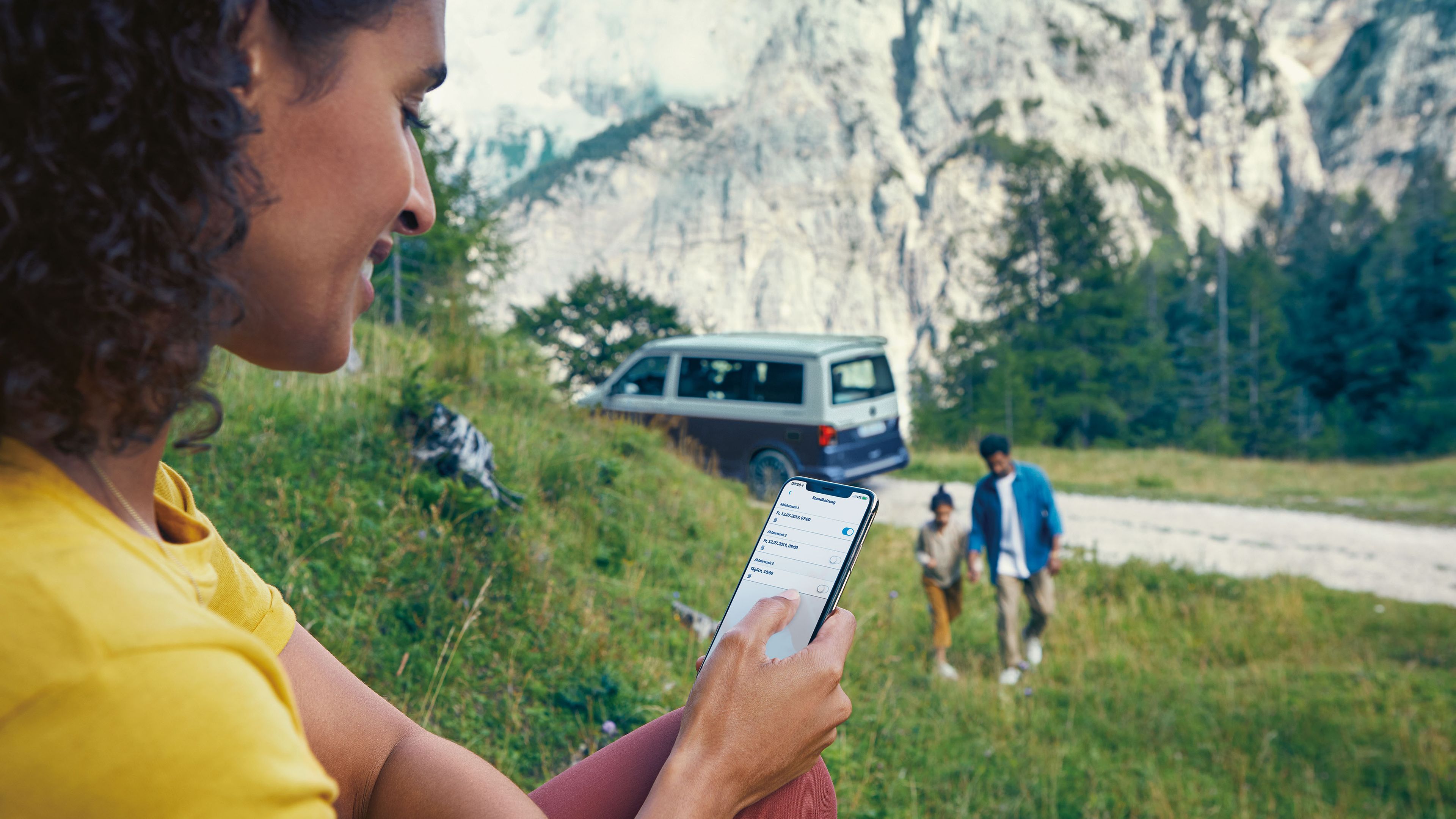 Eine Frau steuert die Standheizung ihres VW California 6.1 über ihr Smartphone mithilfe von We Connect
