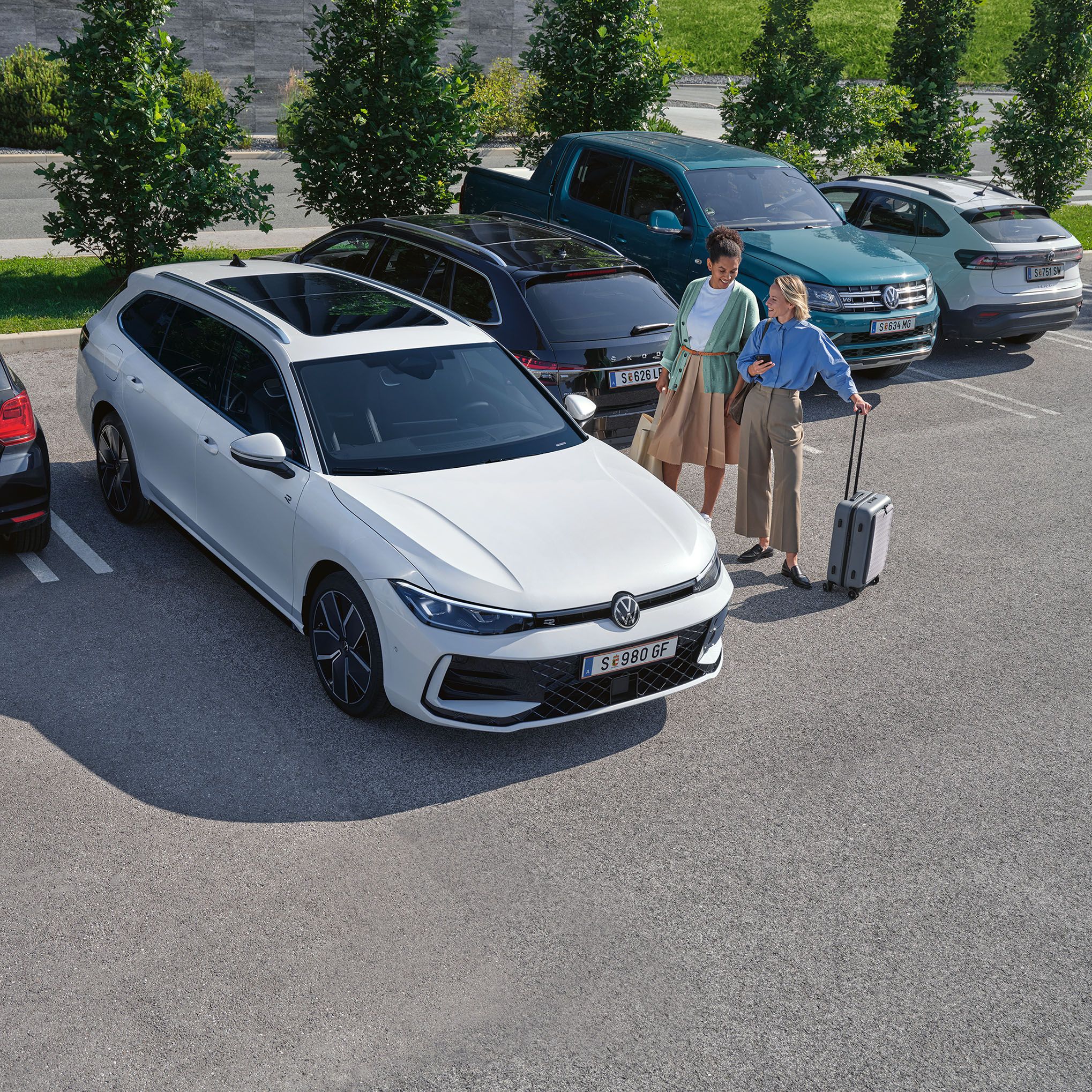 Zwei Frauen stehen neben einem weißen VW Passat R-Line auf einem Parkplatz