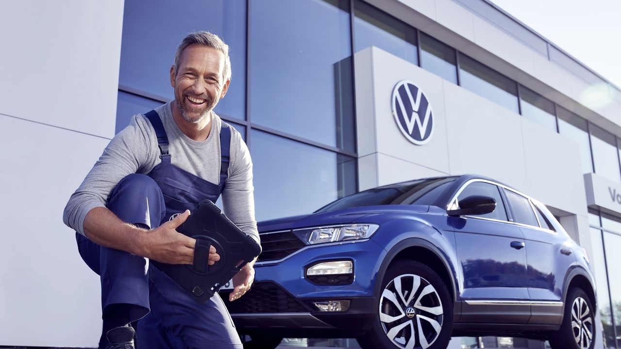 Ein Volkswagen Service Techniker mit Tablet, kniet vor einem blauen Volkswagen T-Roc