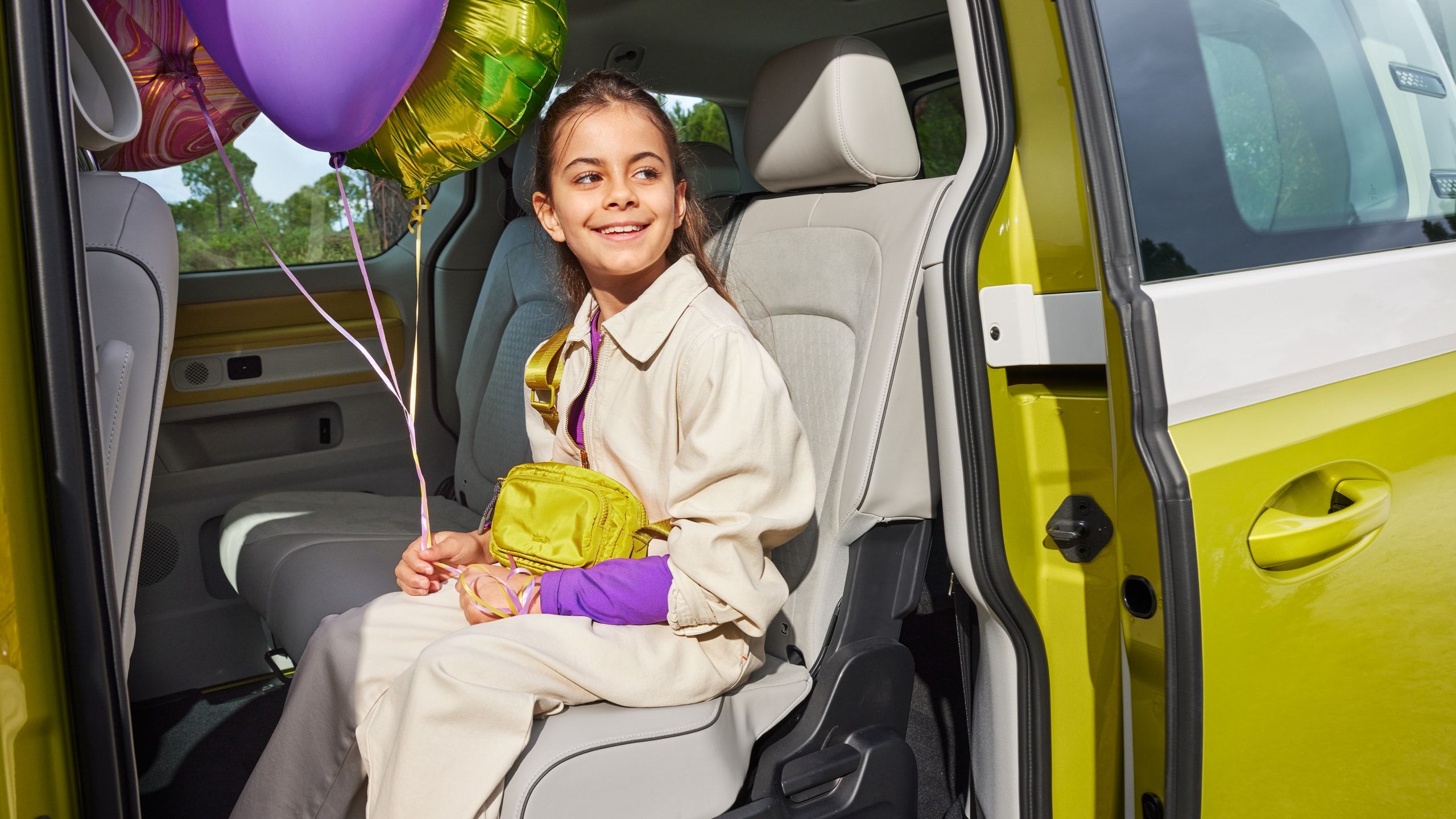 Lächelndes Kind mit Ballons sitzt auf Rücksitz eines gelb weißen ID. Buzz mit offener Schiebetür