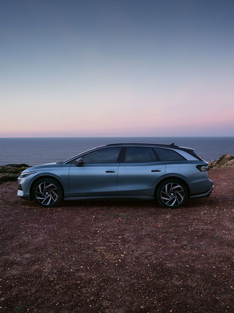 Seitenansicht des VW ID.7 in der Farbe Stonewashed Blue geparkt an der Küste mit Sonnenuntergang