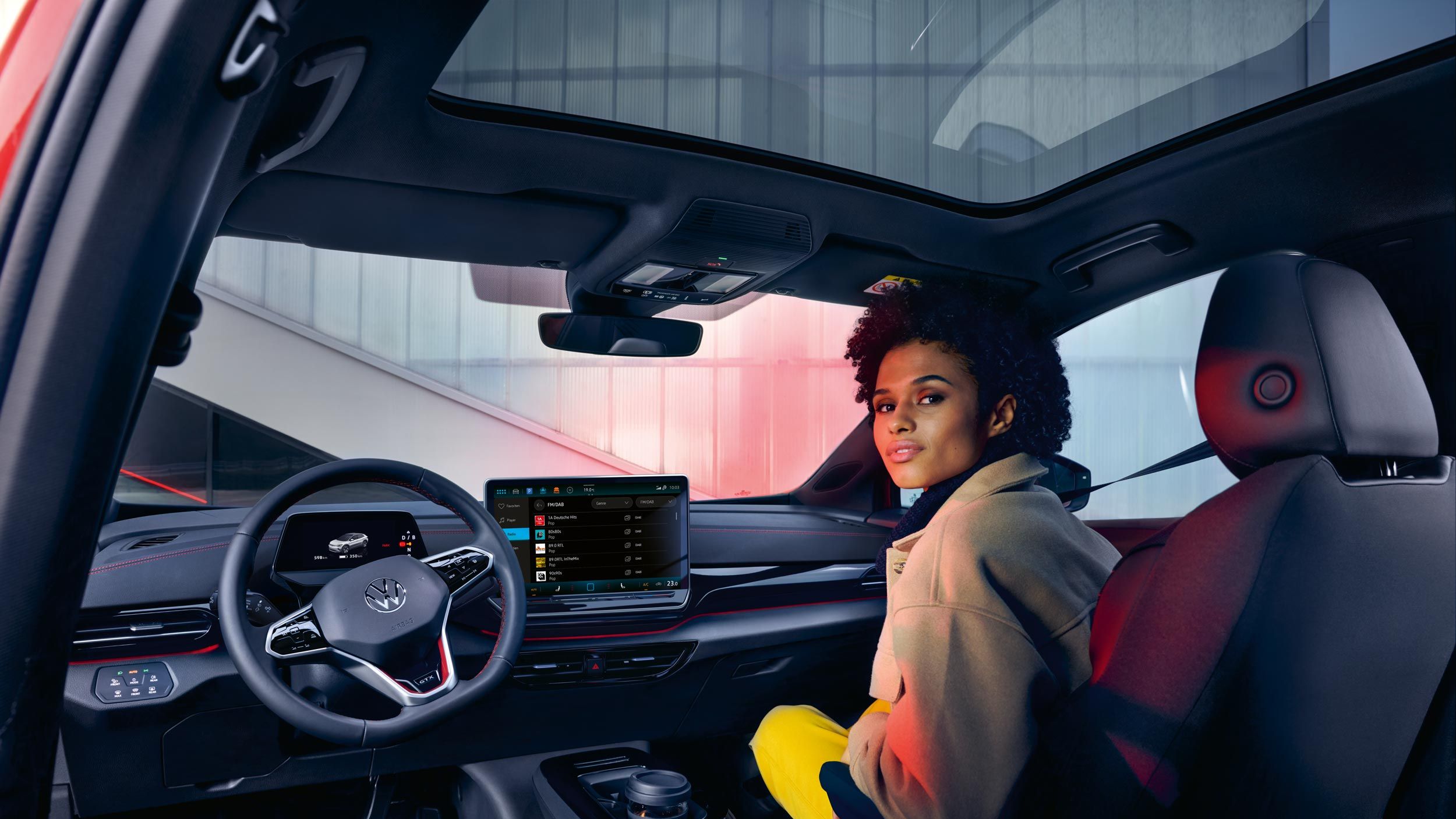 VW ID.4 GTX Innenraum mit Blick auf die Vordersitze und Cockpit. Frau sitzt auf Beifahrersitz mit Blick nach hinten.