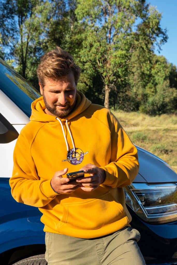 Ein Mann lehnt an seinem VW Nutzfahrzeug und blickt auf sein Smartphone