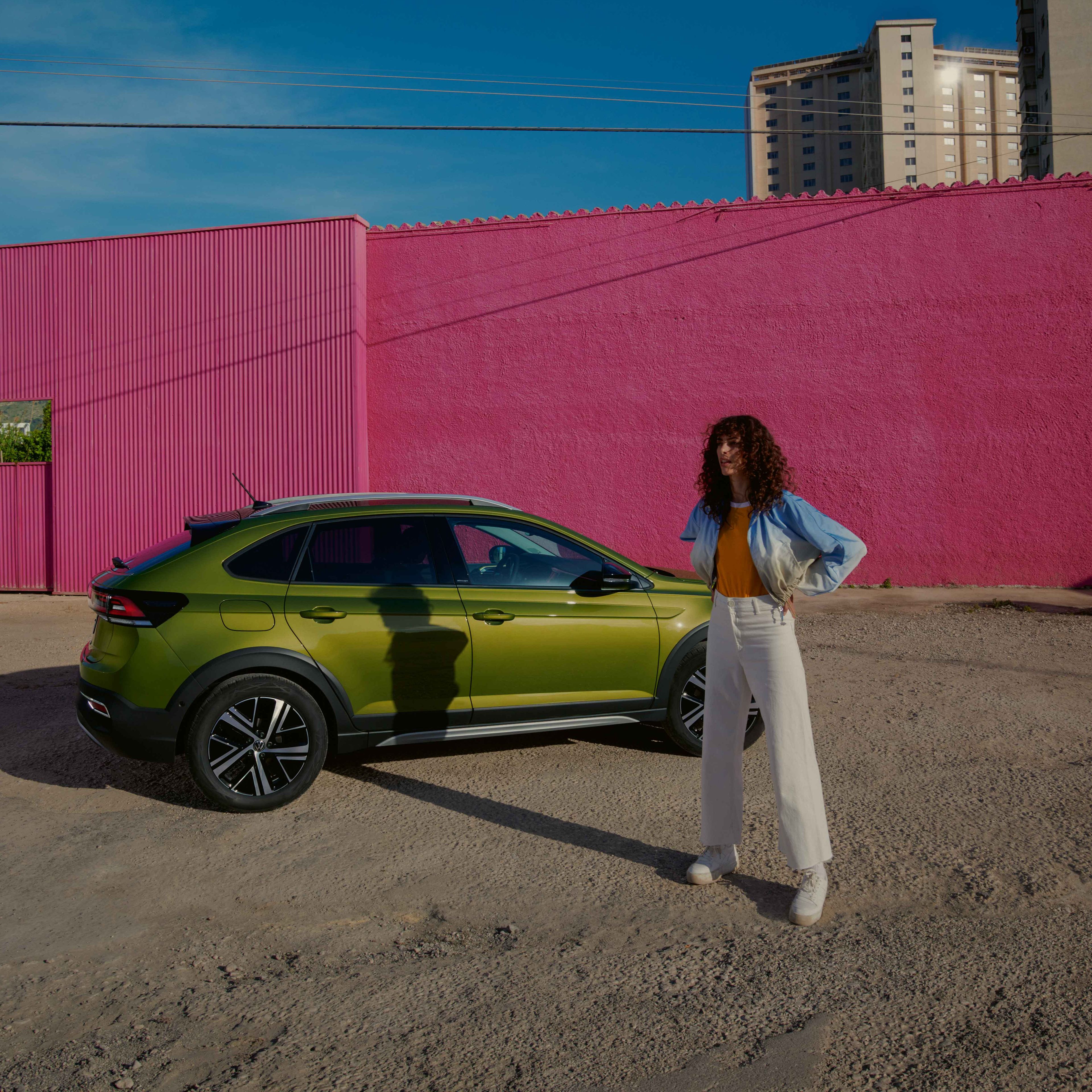 VW Taigo in Grün auf Parkplatz, Seite sichtbar, Frau steht vor Auto