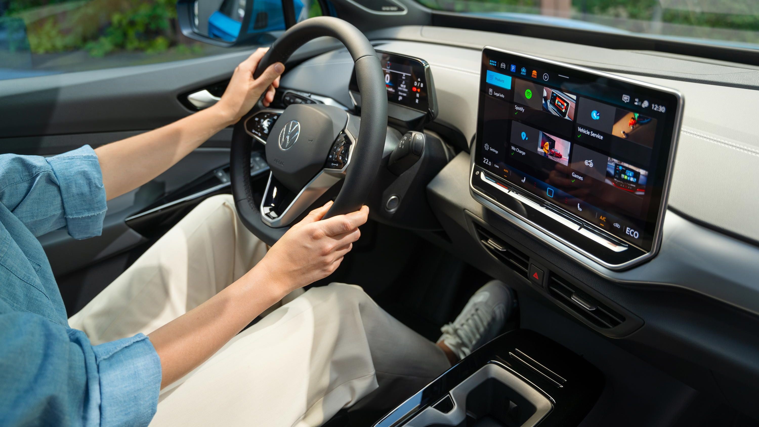 Innenansicht des VW ID.4. Schräger Seitenblick  auf das Multifunktionslenkrad und Infotainmentsystem. Auf dem Fahrersitz sitzt eine Person, die das Fahrzeug lenkt. 