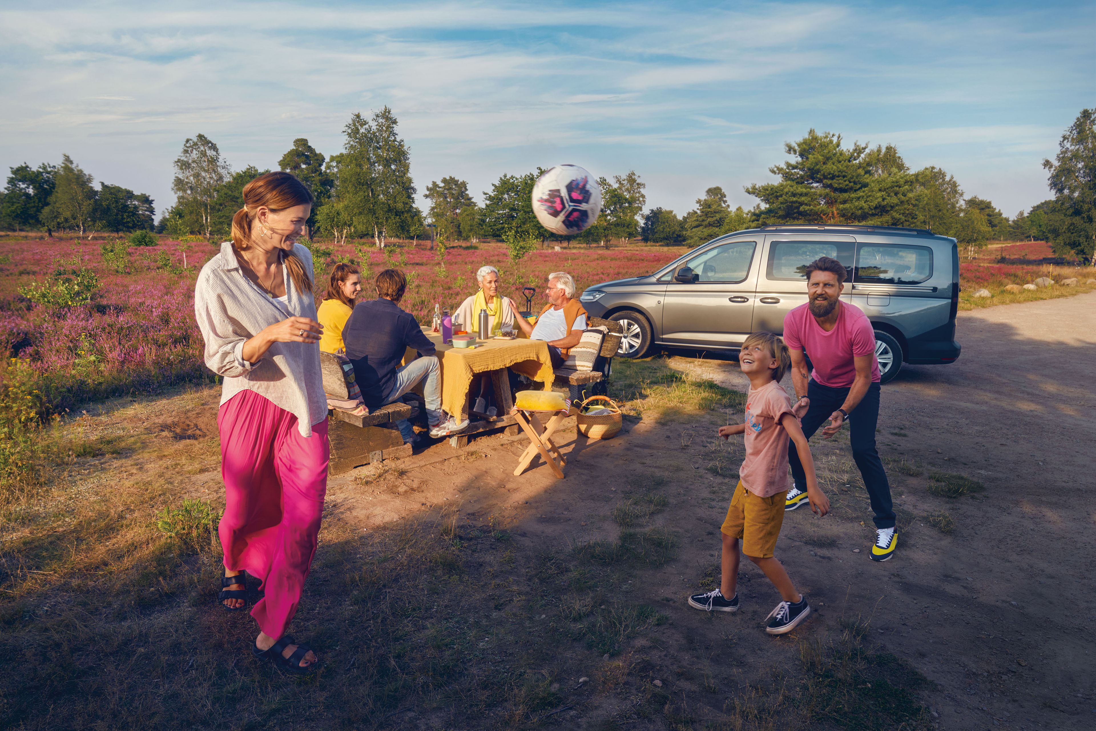 Eine Familie bei einem Picknick, ein VW Caddy parkt im Hintergrund