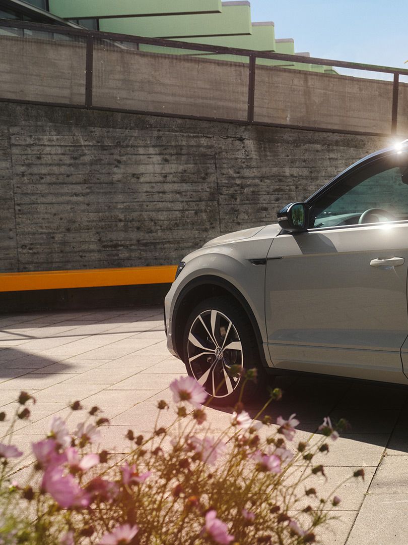 VW T-Roc in weiß parkt auf einem Platz, Ansicht auf die Fahrerseite und das Heck. 