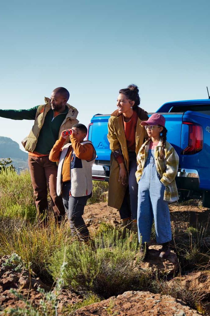 Eine Familie parkt mit einem blauen Amarok in den Bergen und blickt in die Ferne