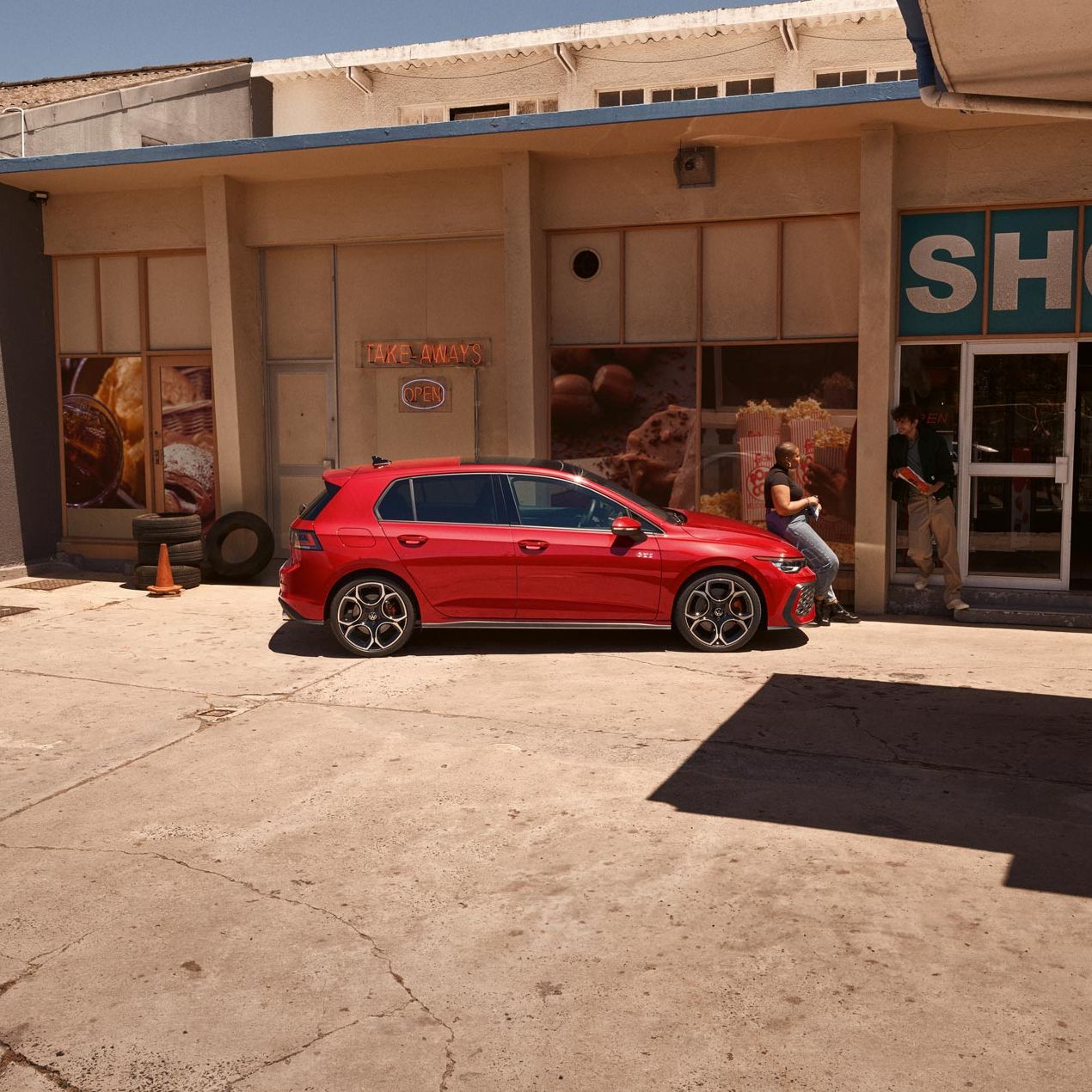 Seitenansicht eines roten VW Golf GTI, Frau lehnt an Motorhaube