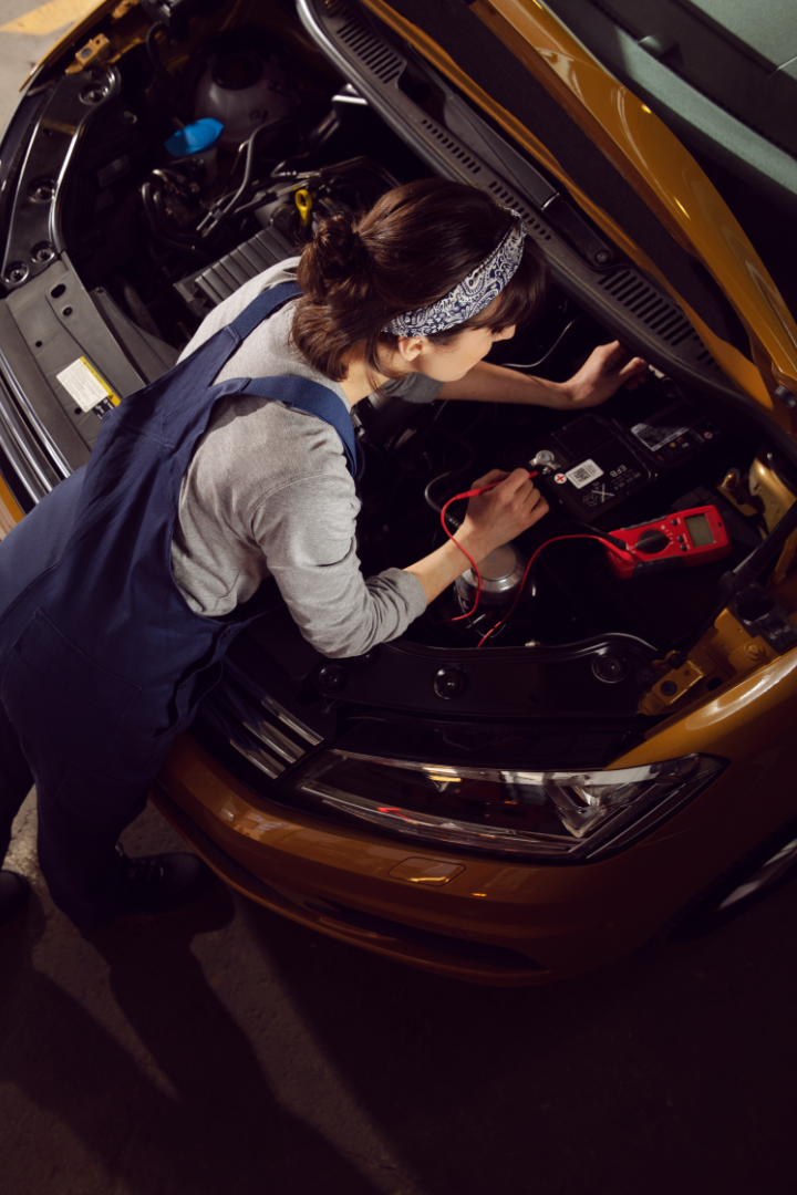 Eine Mechanikerin wechselt eine Batterie bei einem VW Nutzfahrzeug