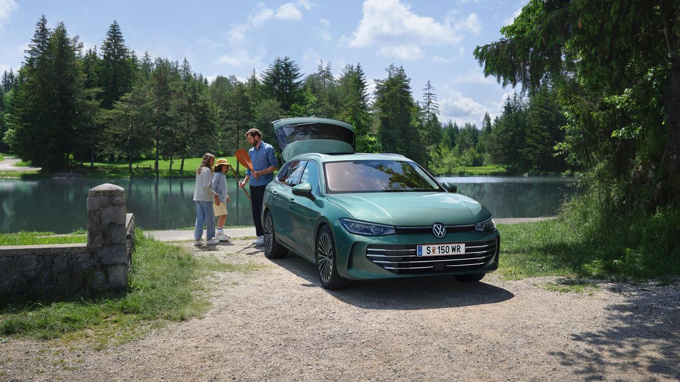 Der neue VW Passat in blaugrün parkt an einem Badesee mit geöffnetem Kofferraum. Ein Mann verteilt Freitzeitspielzeug an zwei Kinder.
