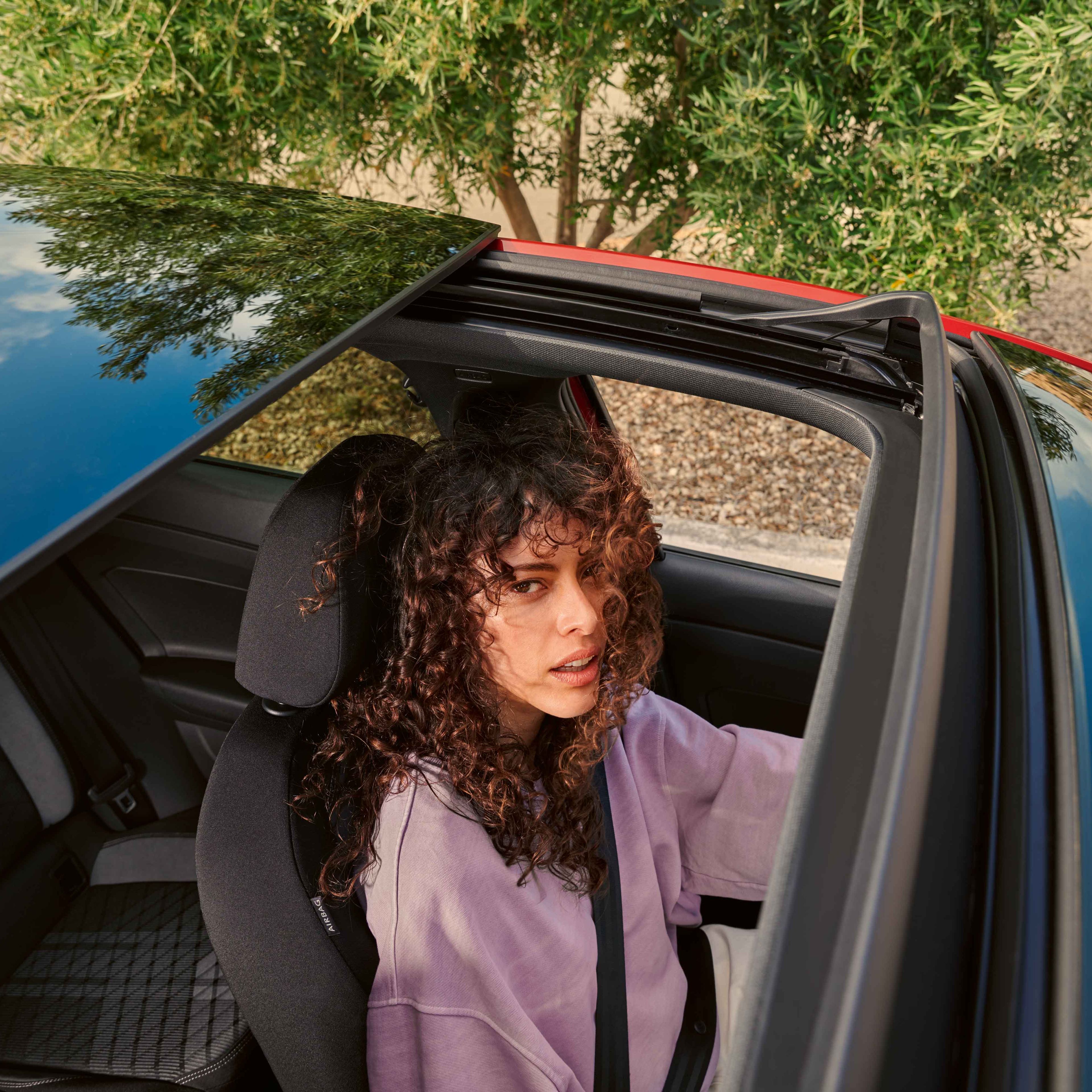 Blick von oben durch das Panoramadach des VW Taigo in dem eine Frau am Fahrersitz sitzt