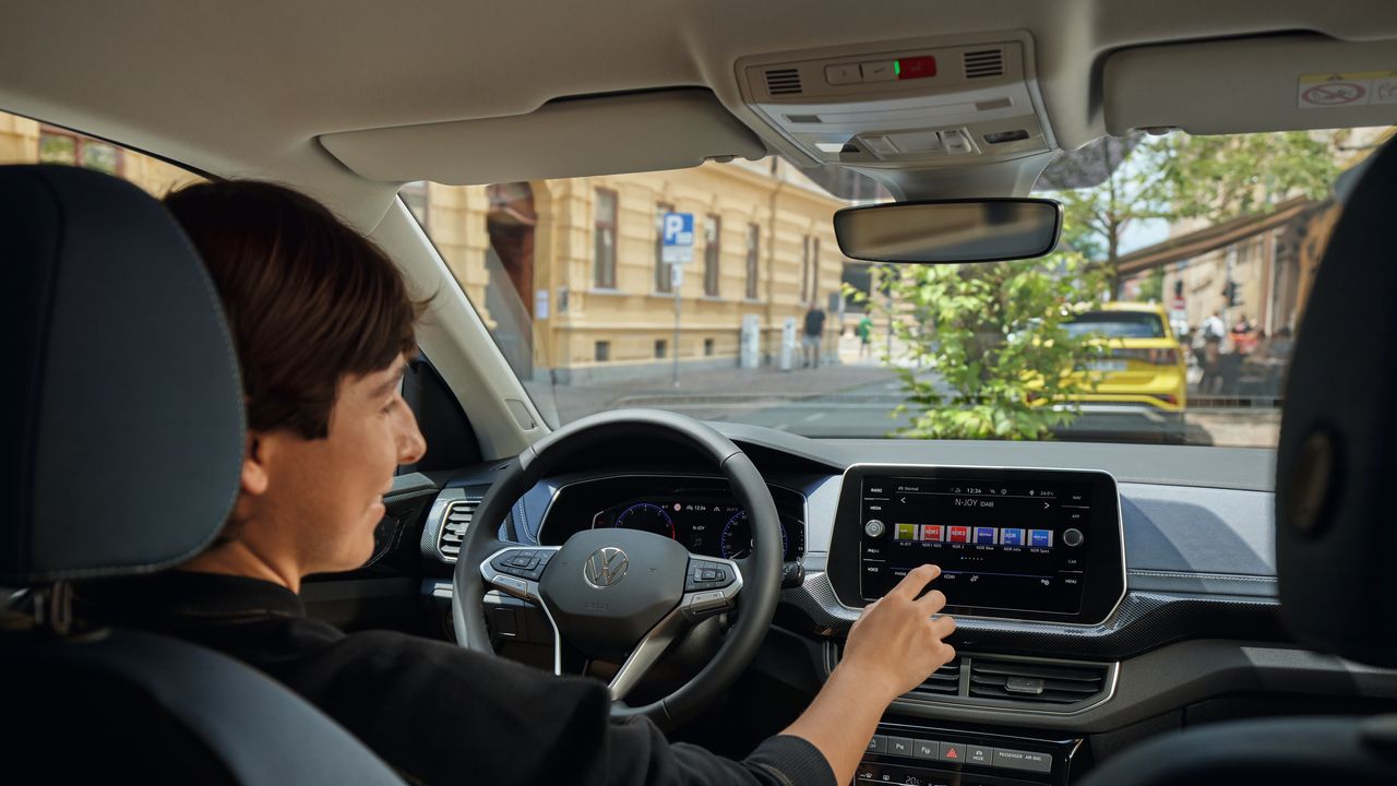 Eine junge Frau bedient vom Fahrersitz aus das Radio über das große Display des Infotainmentsystems des VW T-Cross