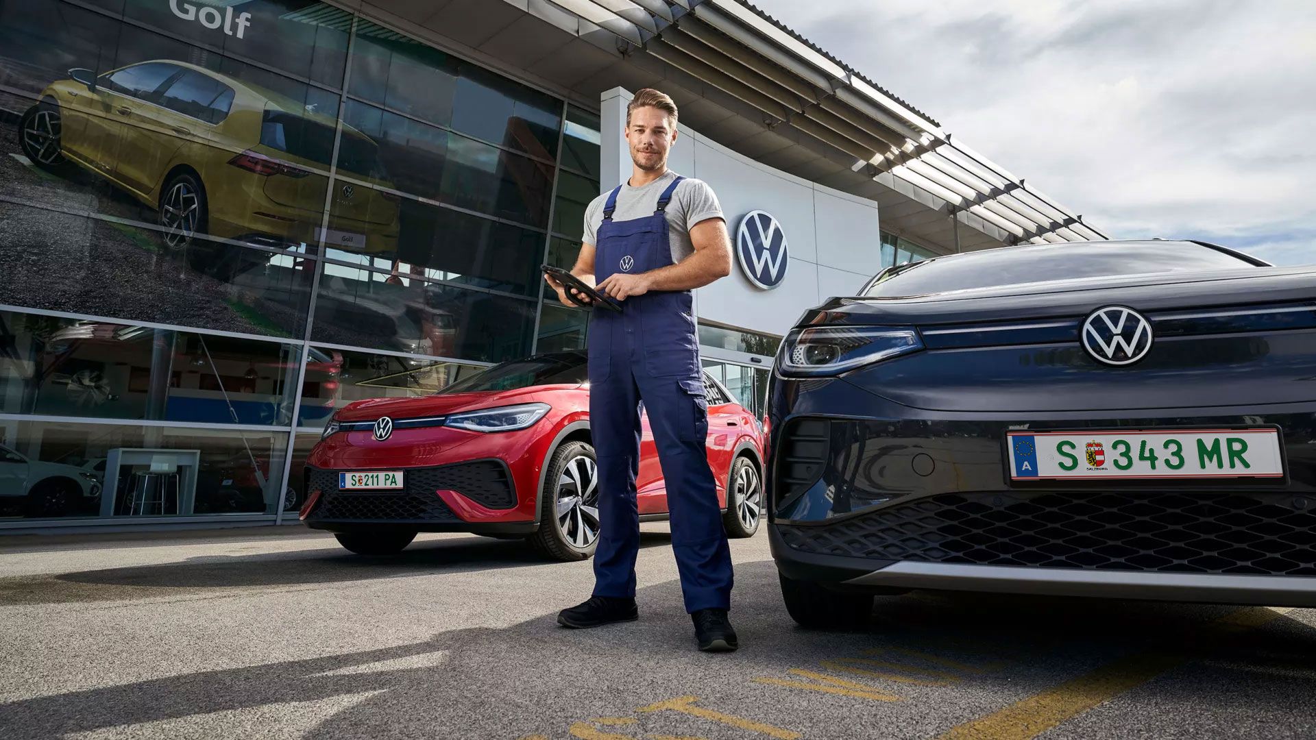 Ein Volkswagen Service Mitarbeiter mit einem Tablet in der Hand steht zwischen einem roten VW ID.5 und einem schwarzen VW ID.4