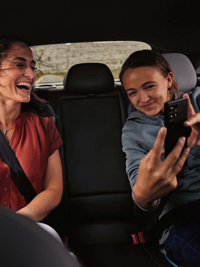 2 Peronen sitzen auf der Rückbank eines Volkswagen und schauen lächelnd auf ein Mobiltelefon