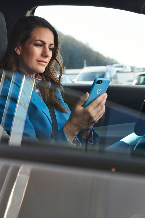 Eine in blau gekleidete Frau sitzt in einem geparkten Volkswagen mit einem Smartphone in ihrer Hand.